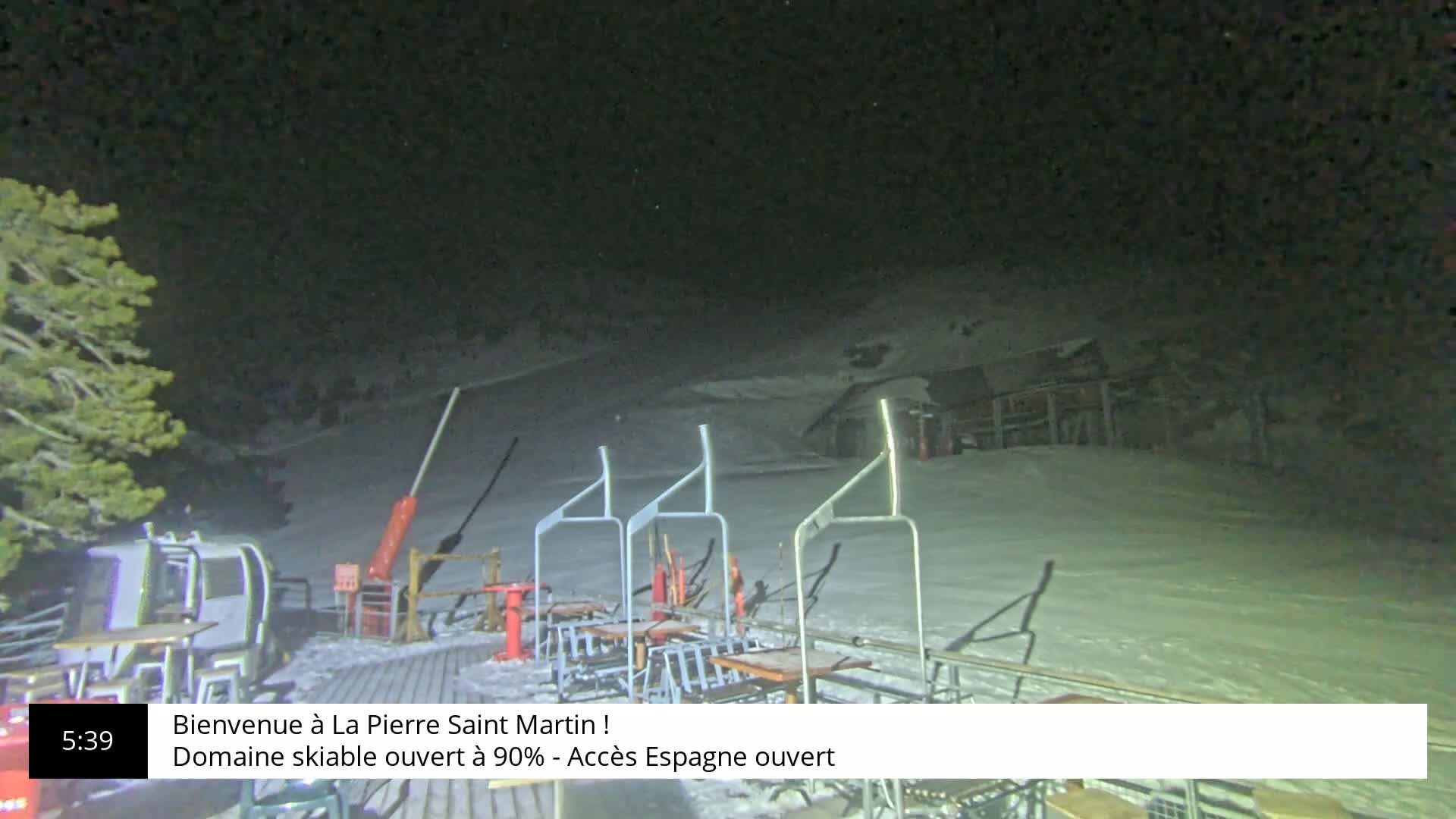 A nighttime view of a snow-covered ski slope with several chairlifts and a small building in the background under a dark sky.