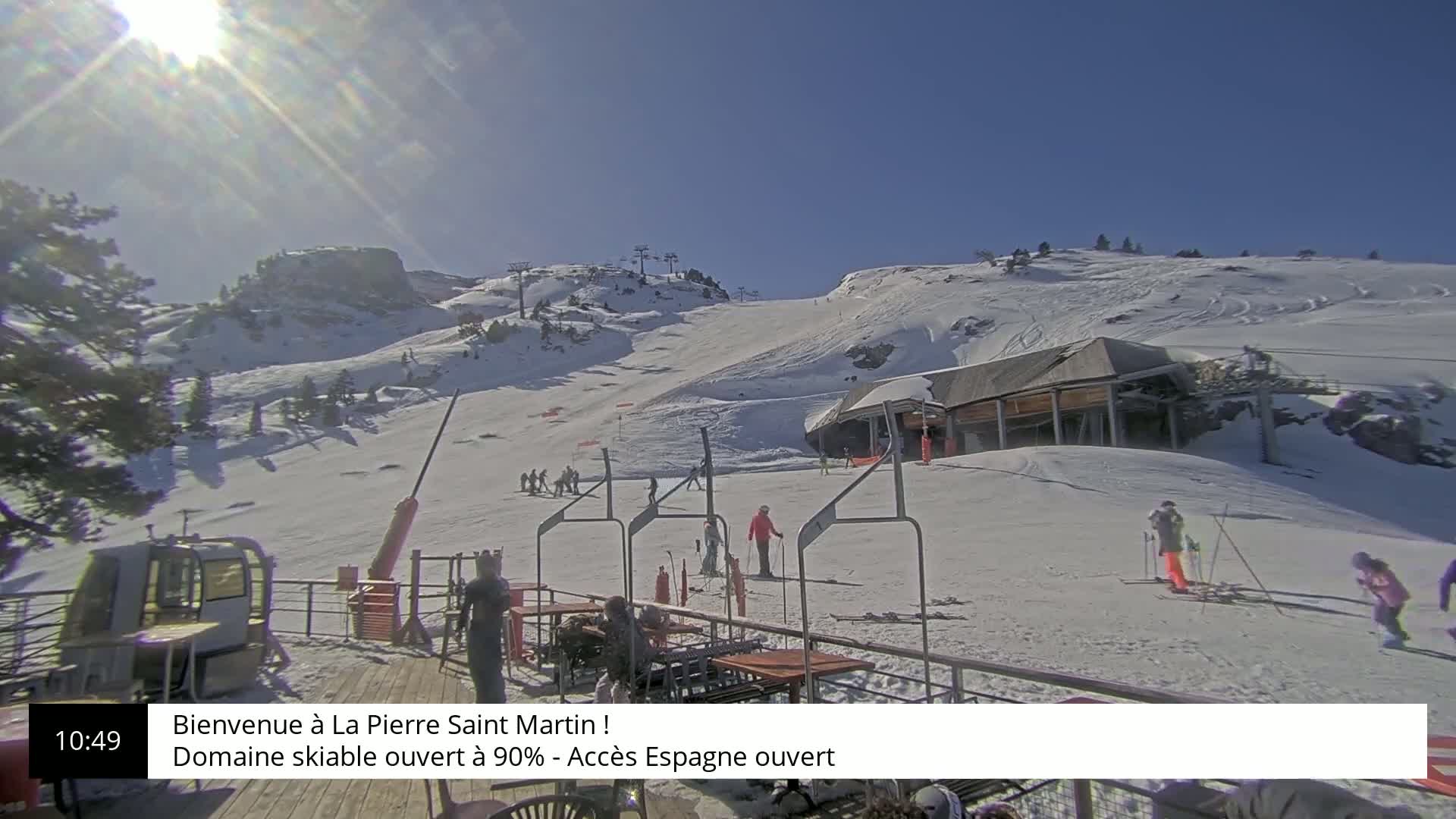A sunny, snow-covered ski slope with several skiers and a ski lift in view.