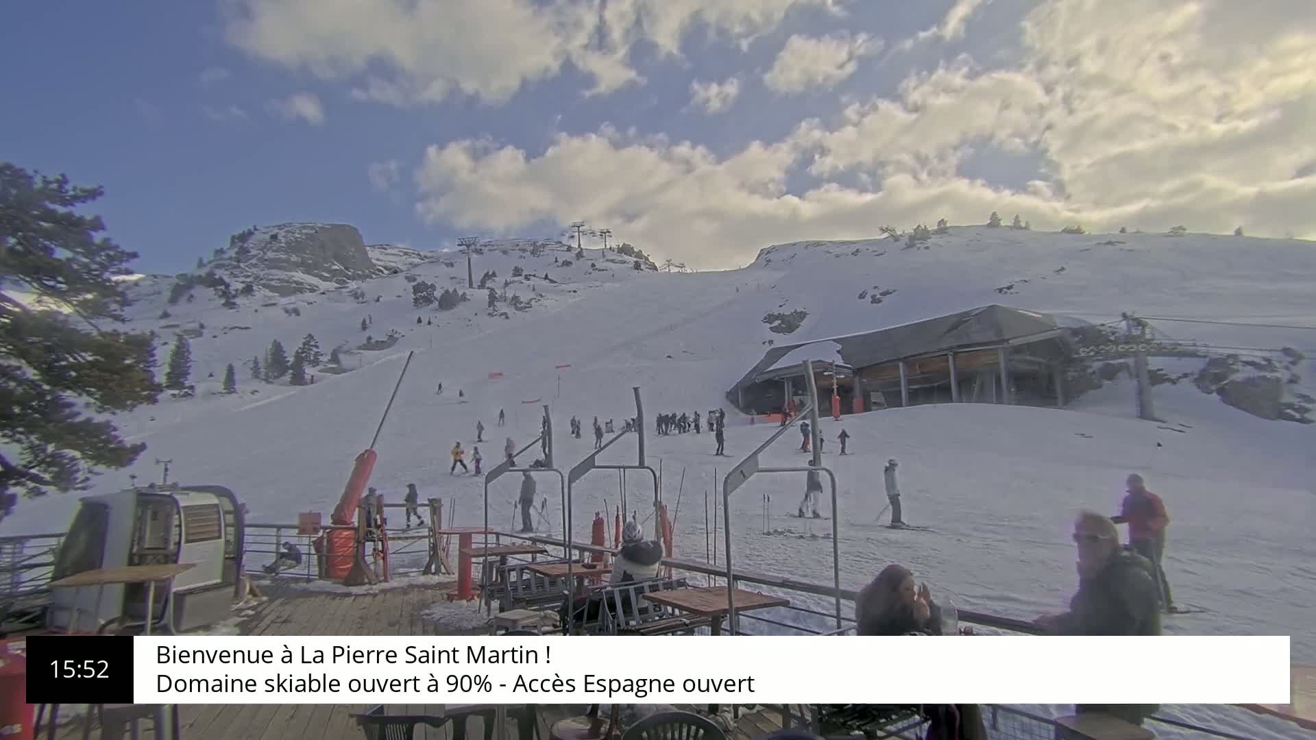 A snow-covered ski slope with skiers and a ski lift, under a partly cloudy sky.