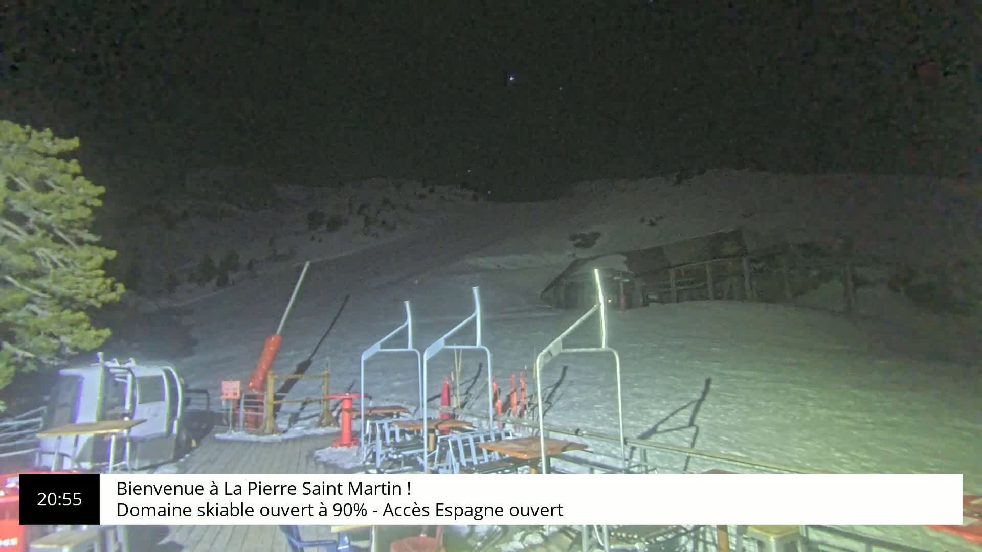 A nighttime view of a snow-covered ski slope with chairlifts and a building under a clear, starry sky.