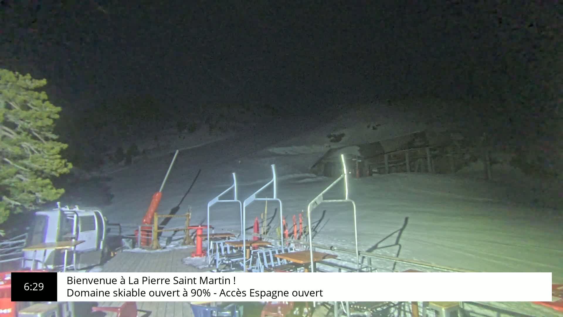 A nighttime view of a snow-covered ski slope with a chairlift and some outdoor furniture.