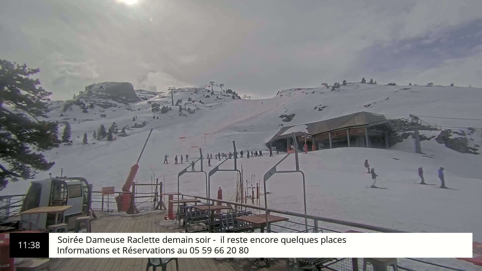 A snowy ski slope with a ski lift and several skiers visible on a partly sunny day.