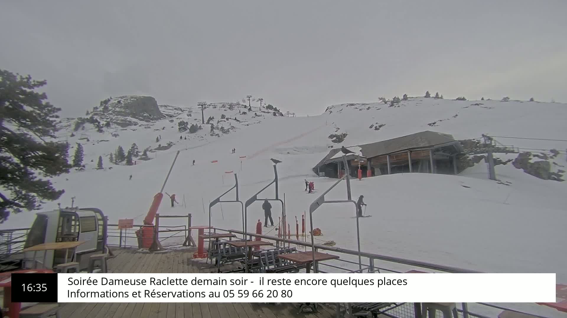 A snowy ski slope with a few skiers and a ski lift, under an overcast sky.