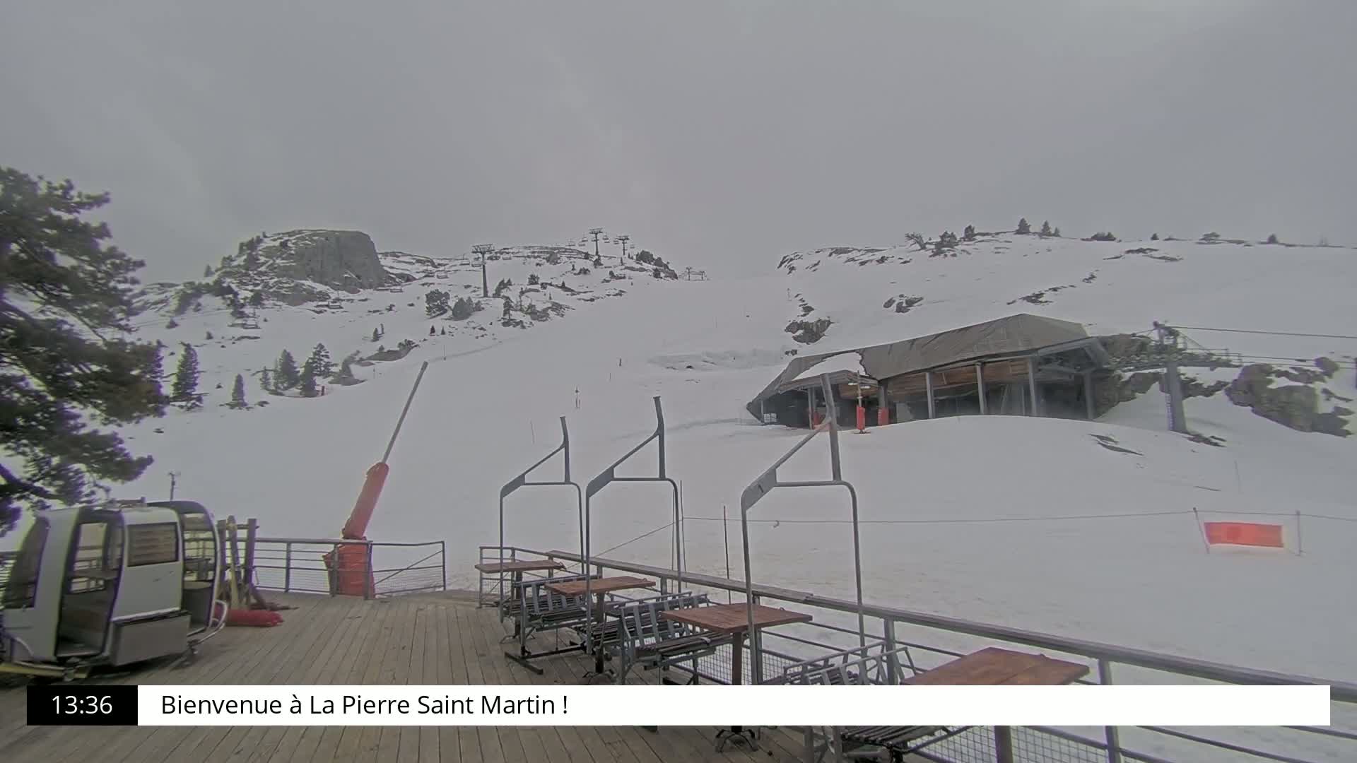 A snow-covered ski slope with a chairlift and a small building is visible under an overcast sky.