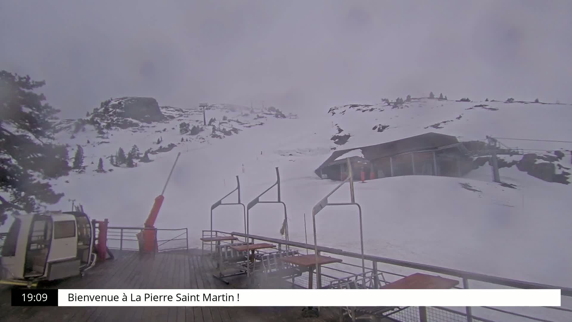 A snowy mountain slope with a chairlift and a building is visible on an overcast day.