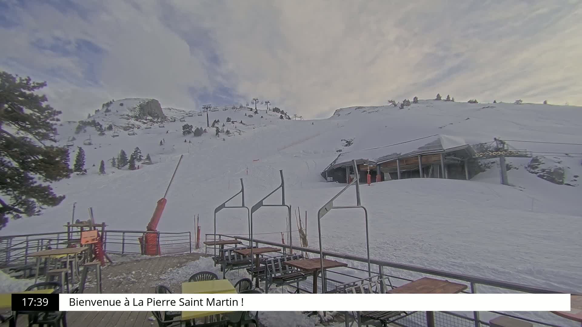 A snow-covered ski slope with a ski lift and outdoor seating area under a cloudy sky.
