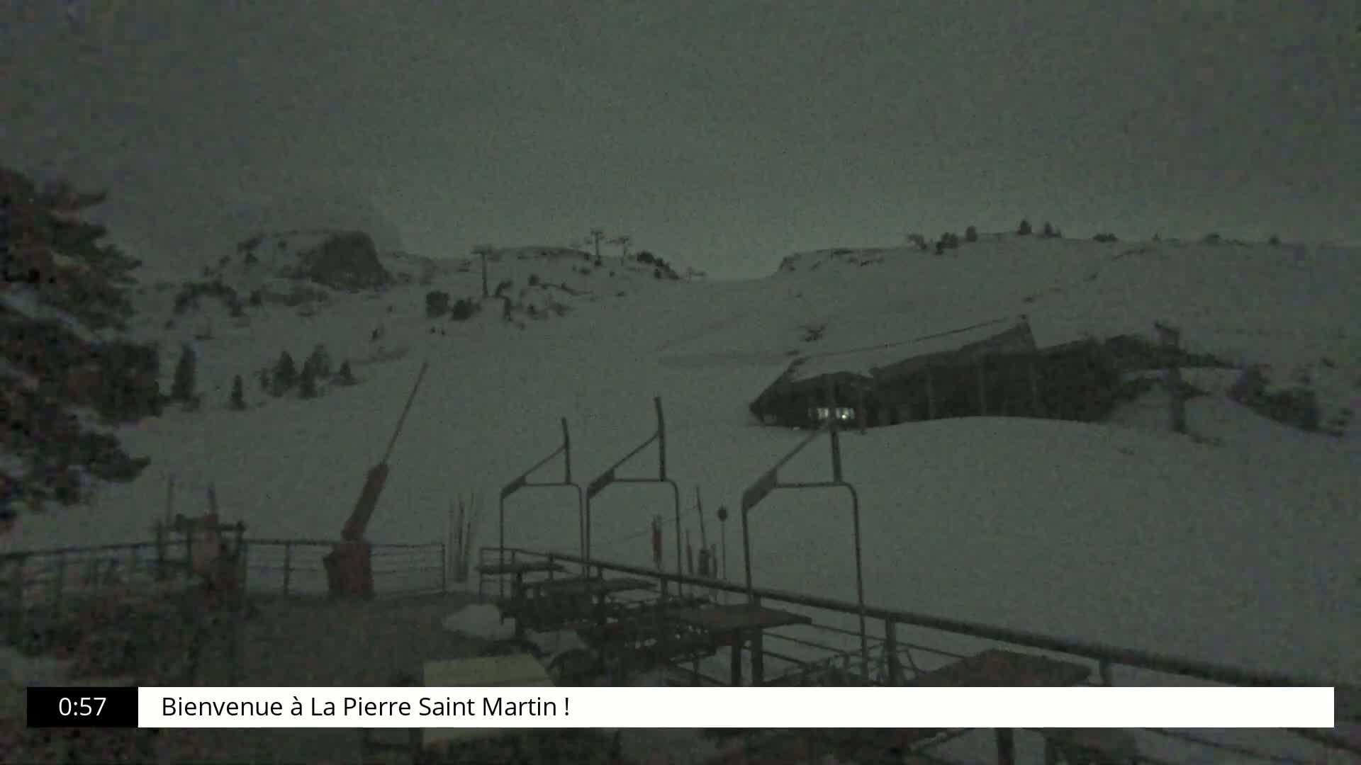A snow-covered ski slope is visible at night under a dark, possibly snowy sky, with a building and ski lift visible in the midground.