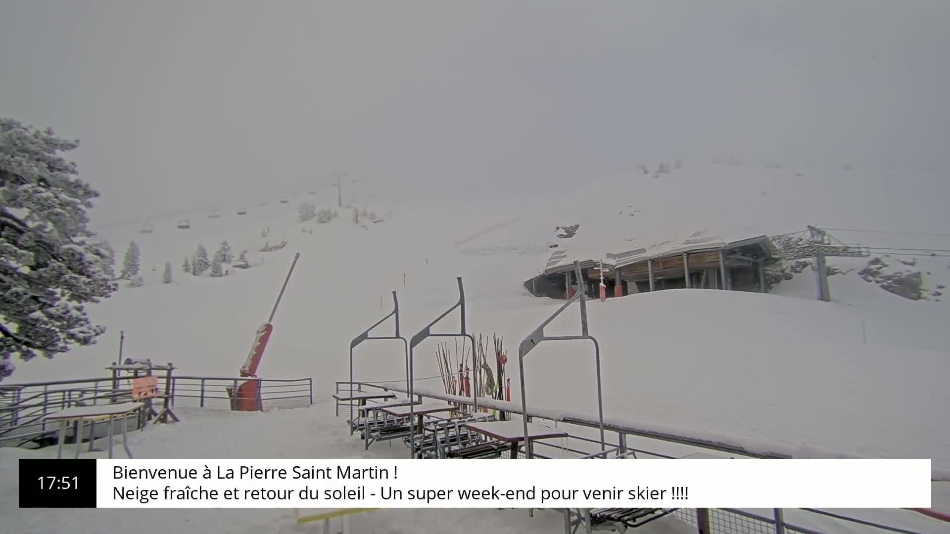 A snow-covered ski resort with a chairlift and a building in the background under hazy conditions.