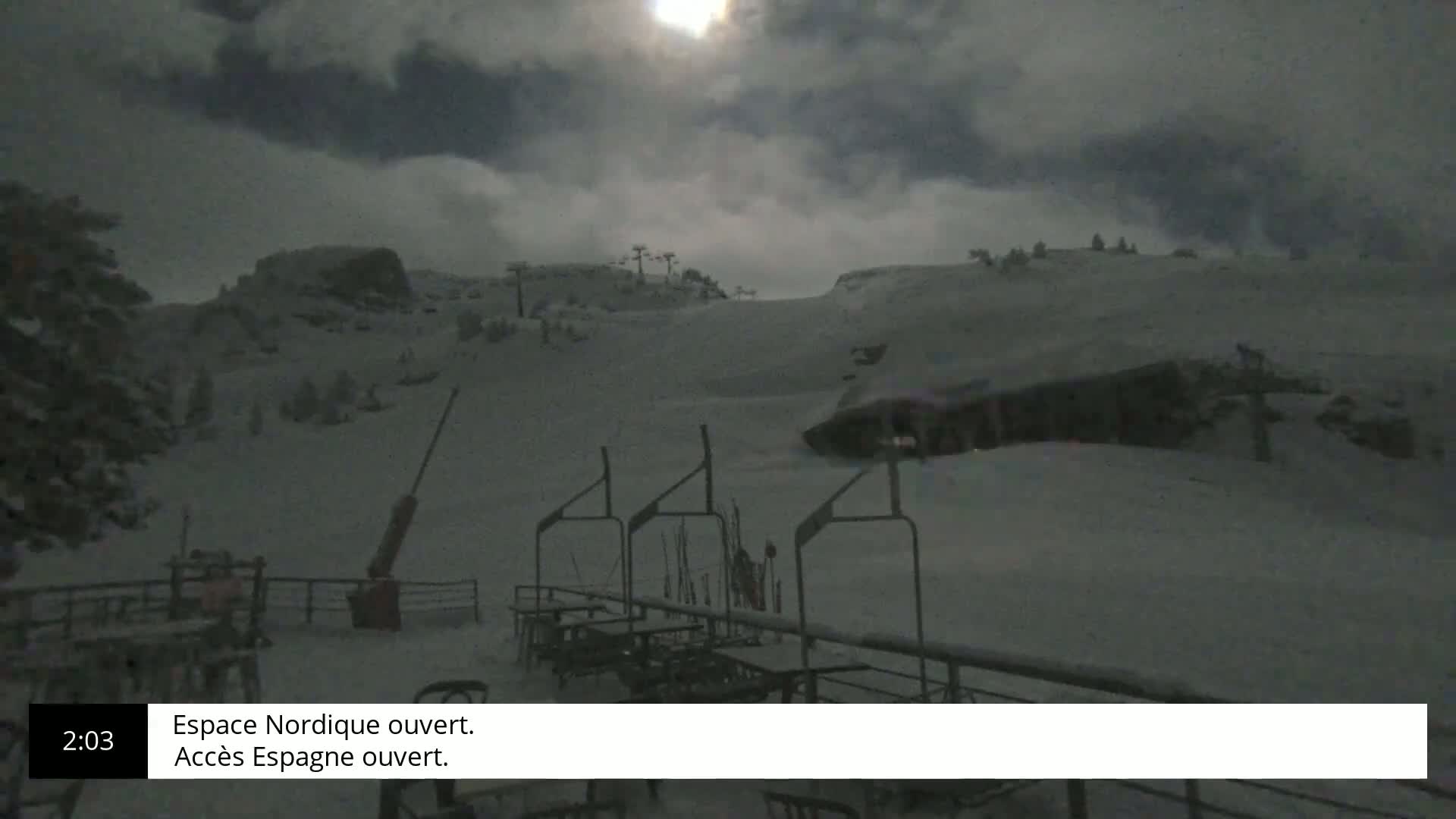 A moonlit snowy landscape at night shows a ski slope with several ski lifts and outdoor seating.