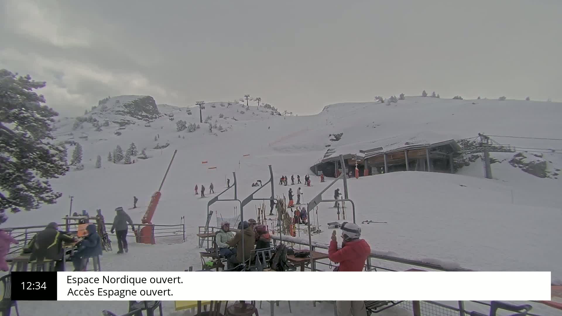 A snowy ski slope with several skiers and snowboarders, a ski lift, and a small building under an overcast sky.