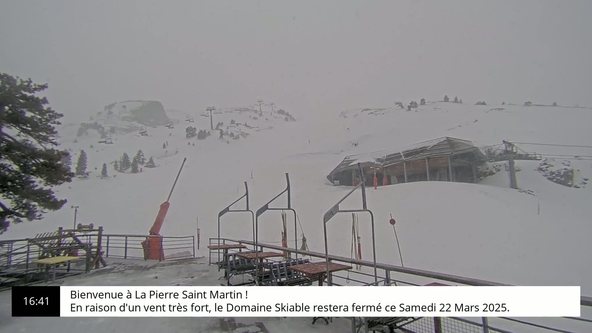 A snow-covered ski slope is seen on an overcast day, with a ski lift and chairlift in the foreground.