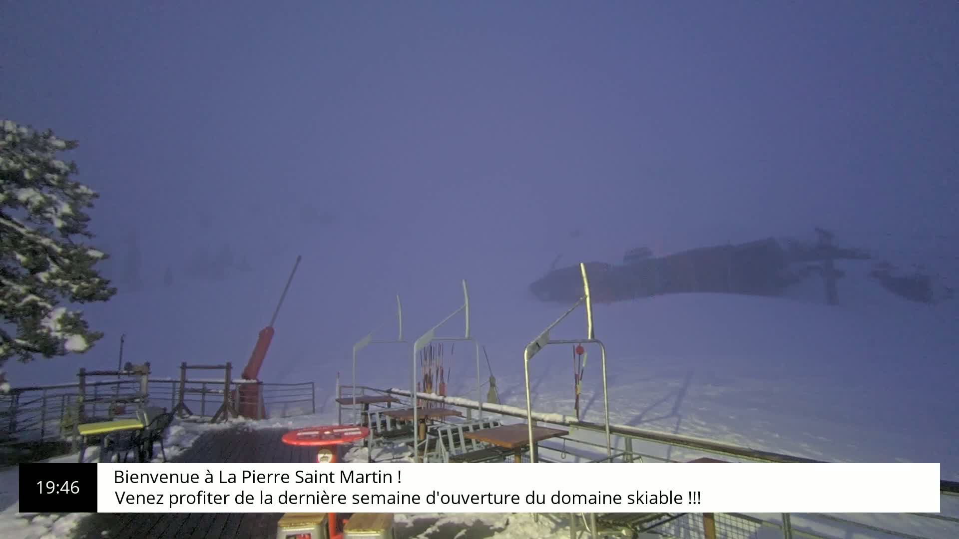 A snow-covered outdoor scene is shrouded in heavy fog, showing a ski lift and outdoor seating area.