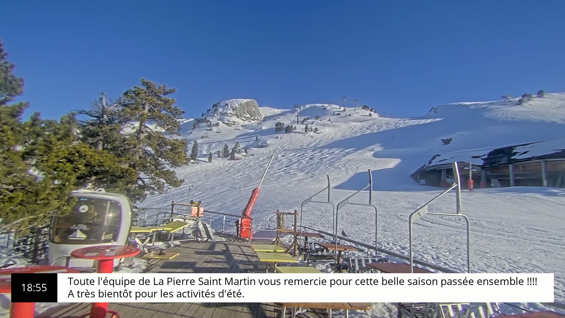 A sunny, snow-covered ski slope with several ski lifts and an outdoor patio area with tables and chairs is visible.