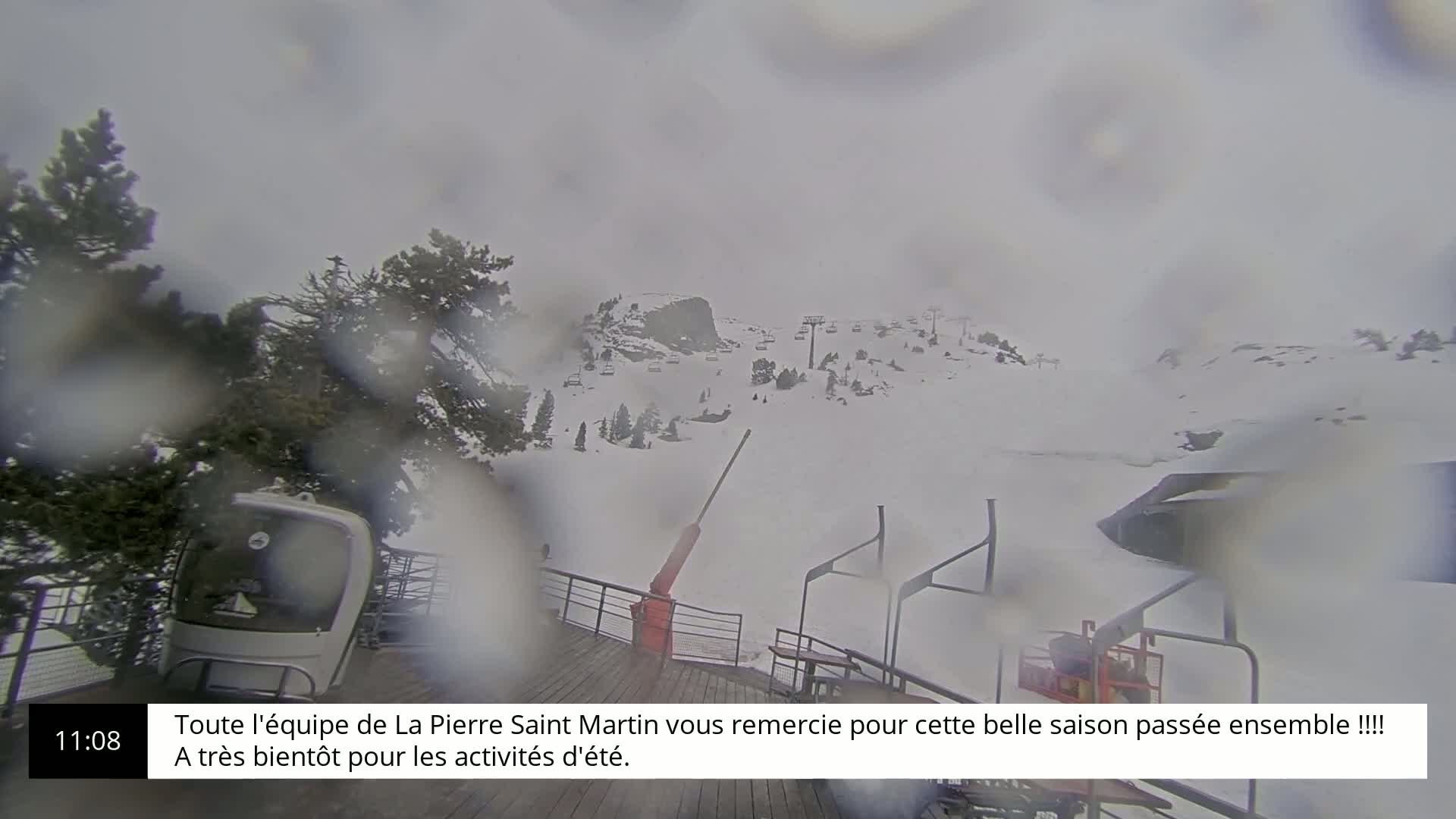 A snowy ski resort is viewed through rain-covered glass, showing a chairlift and several ski runs.
