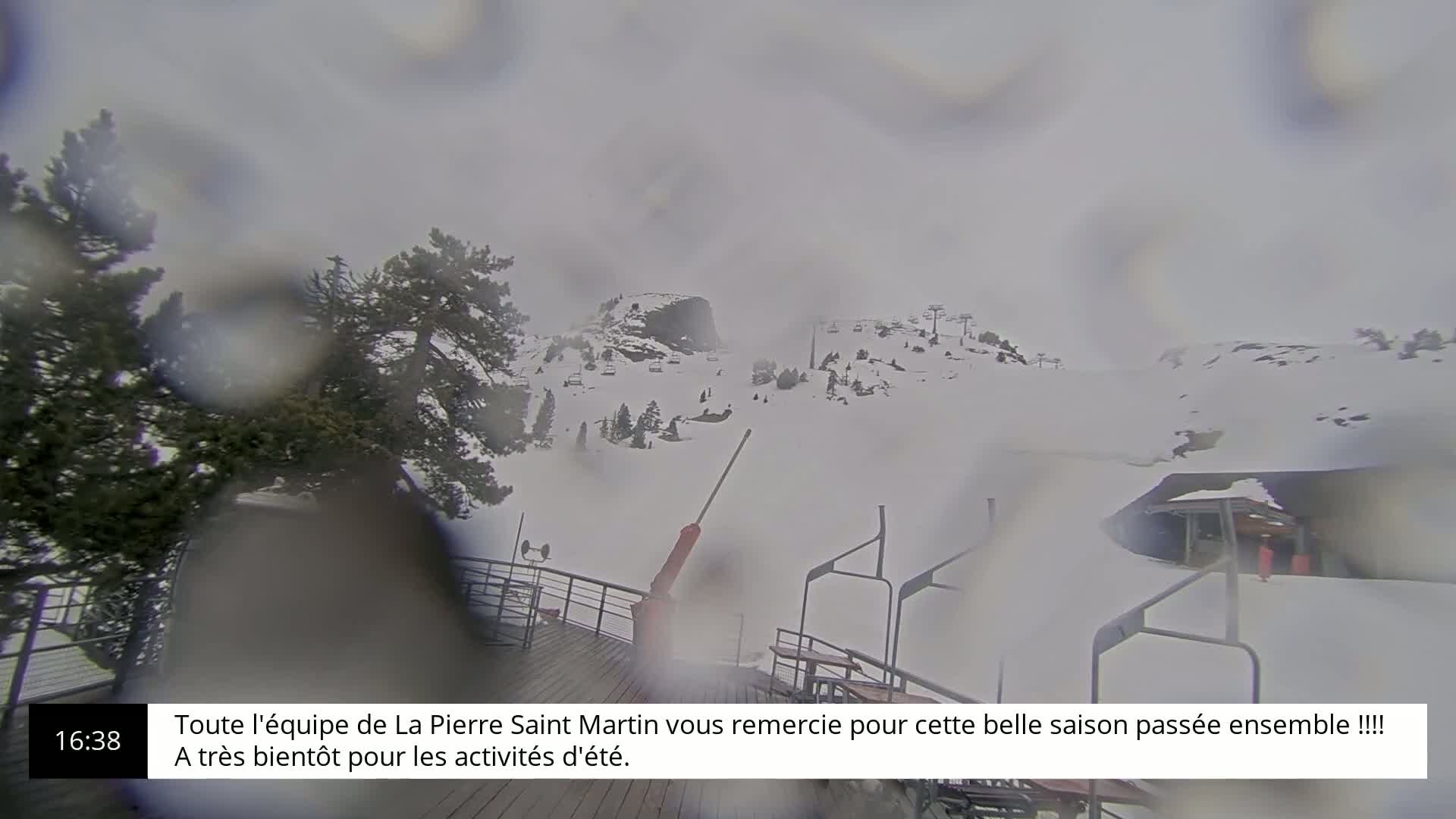 A snow-covered ski resort is seen through rain-covered glass, with a chairlift and several buildings visible in the distance.