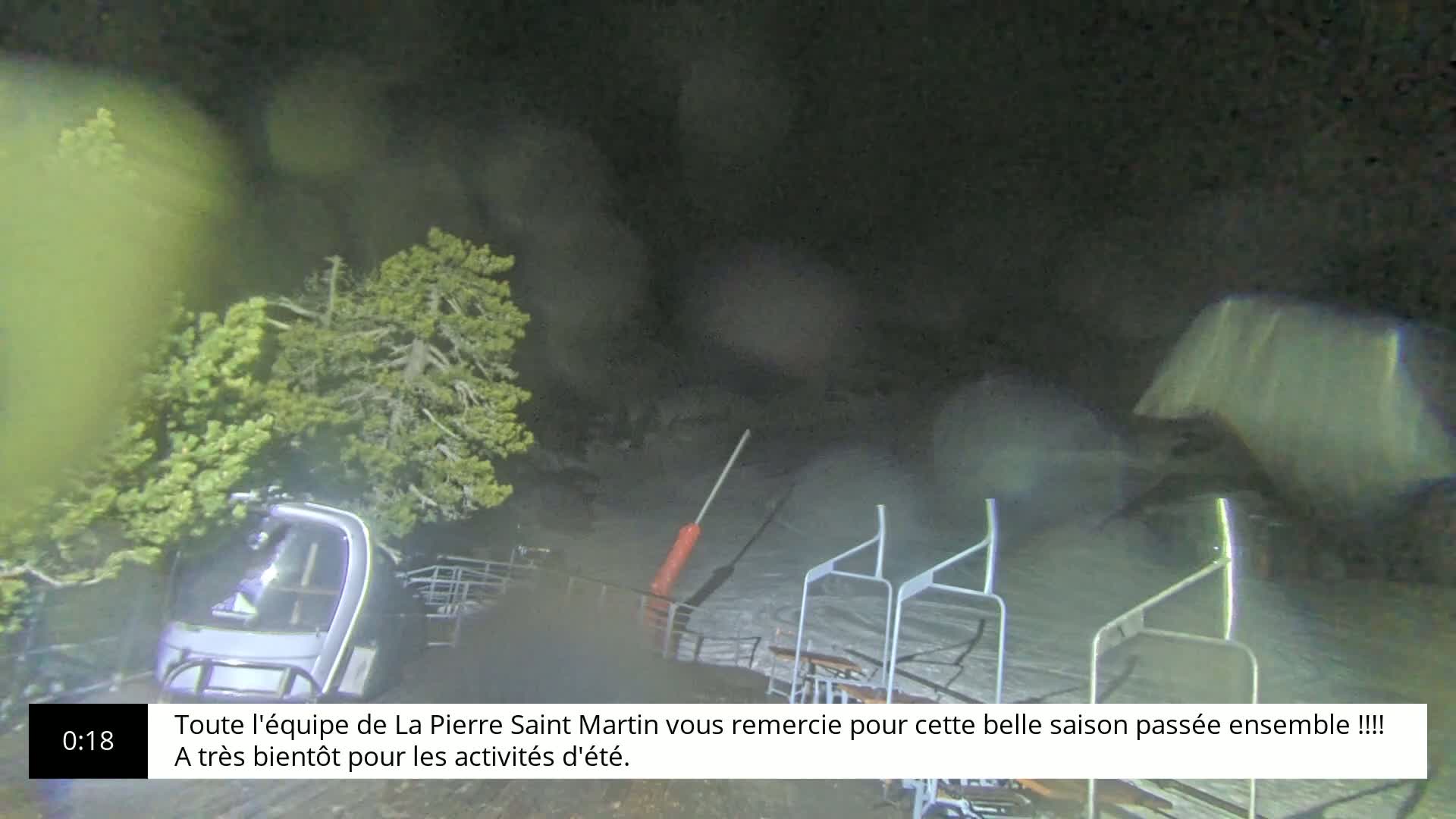 A nighttime, snowy scene shows a chairlift with its chairs down and a snowcat overturned near some trees.