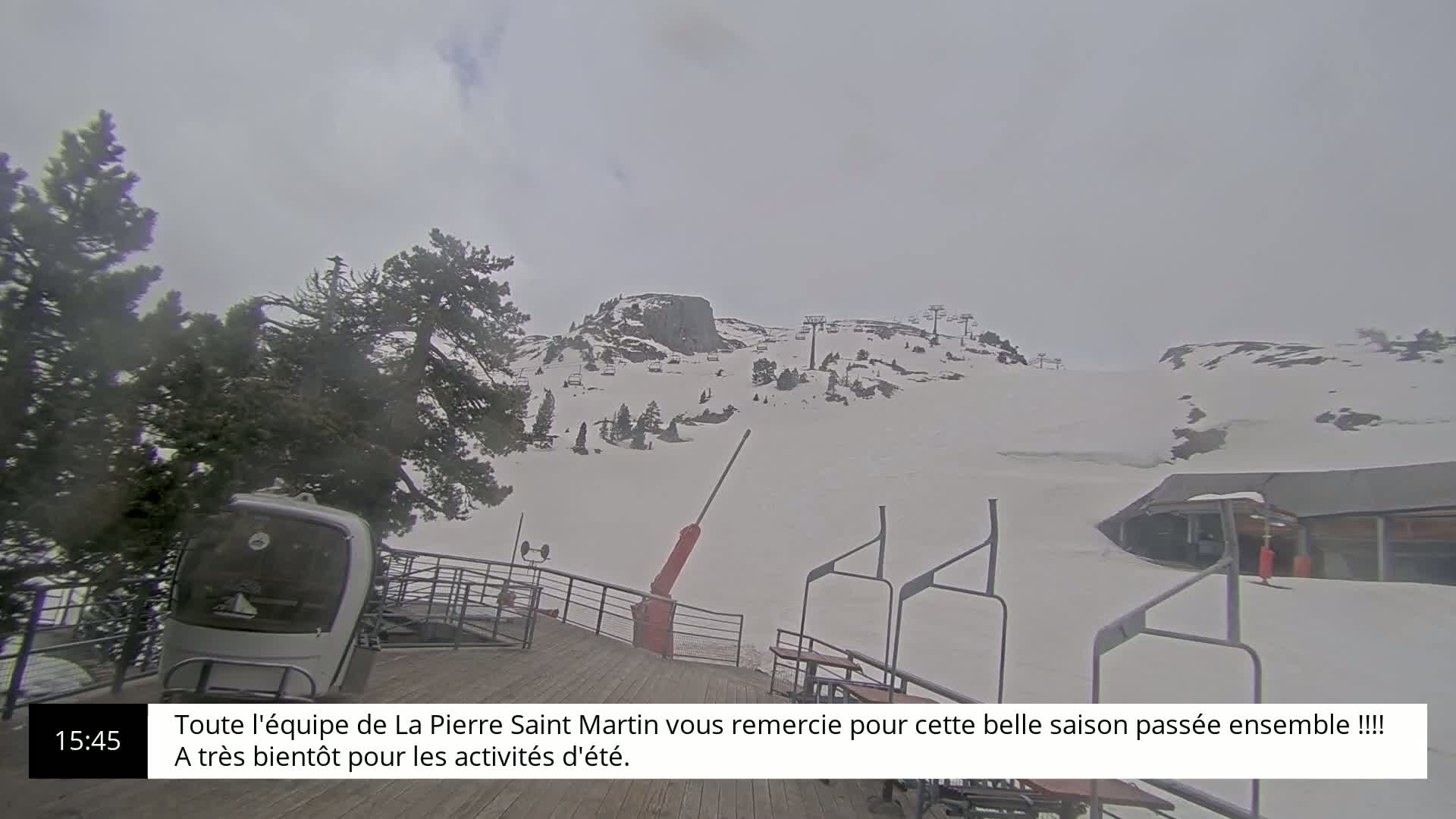 A snow-covered ski slope is seen from a deck with a chairlift in the foreground on an overcast day.