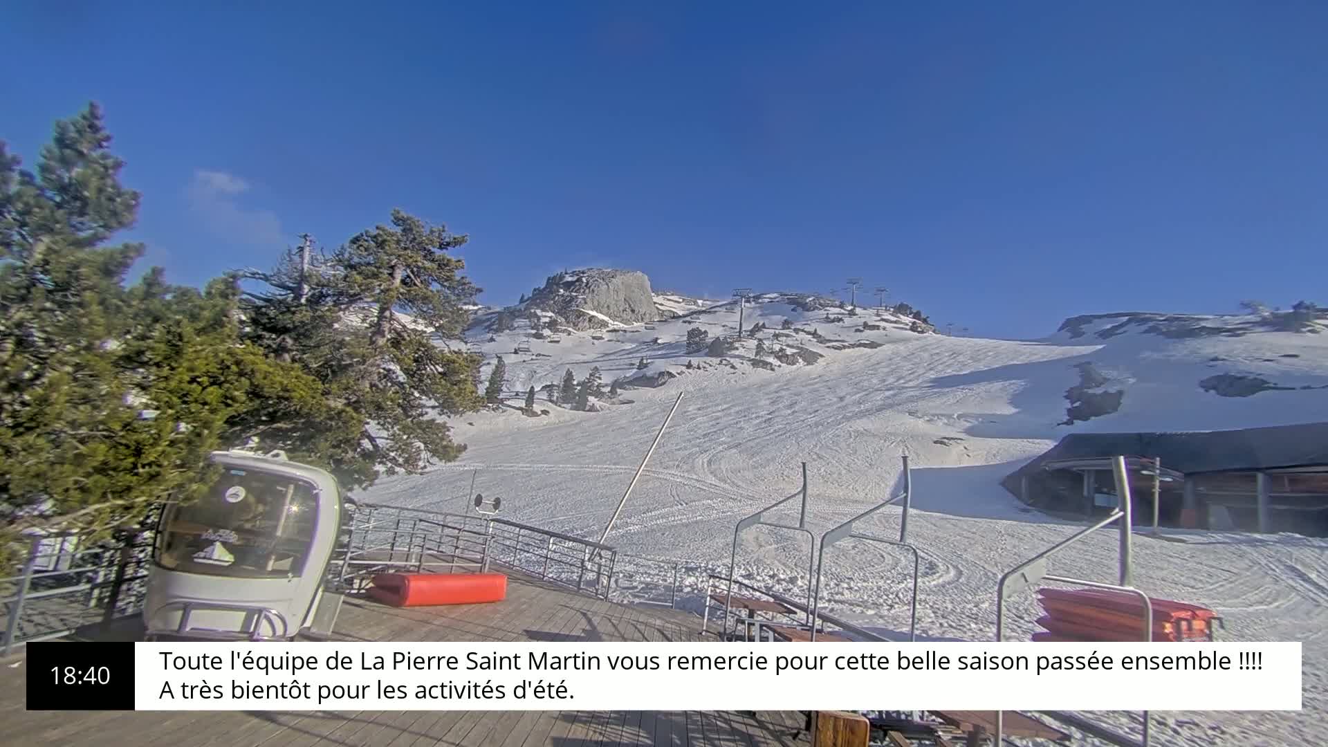 A snow-covered ski slope with a clear blue sky stretches towards a mountain peak under sunny conditions.