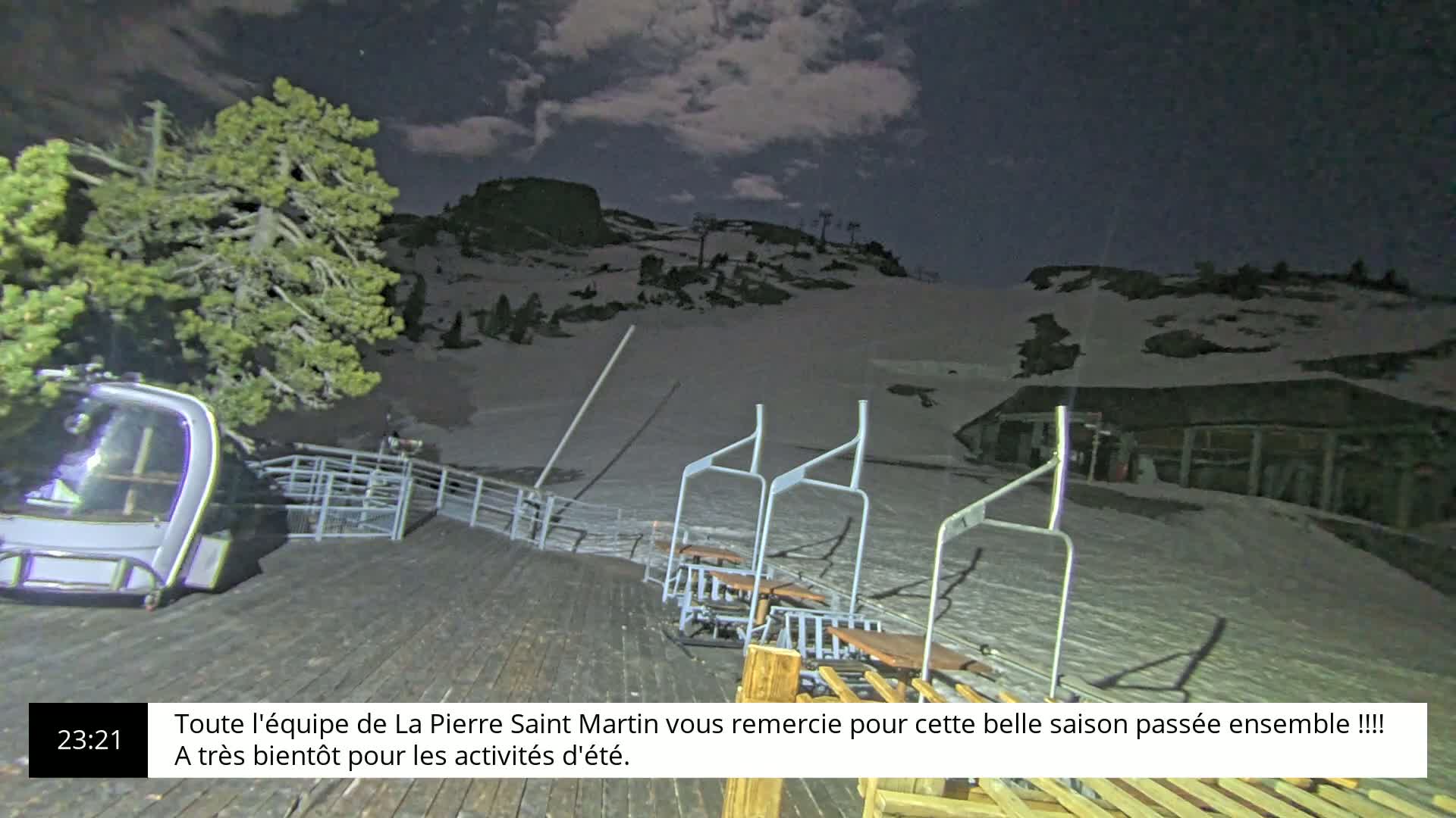 A nighttime view of a snow-covered ski slope with a chairlift and a gondola at the base under a partly cloudy sky.