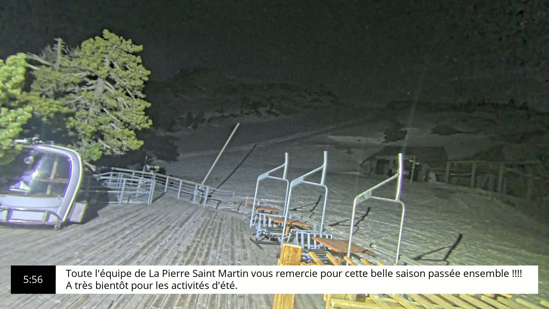 A nighttime view of a snow-covered ski lift and empty chairlift with a single chair at the bottom, under a dark sky.