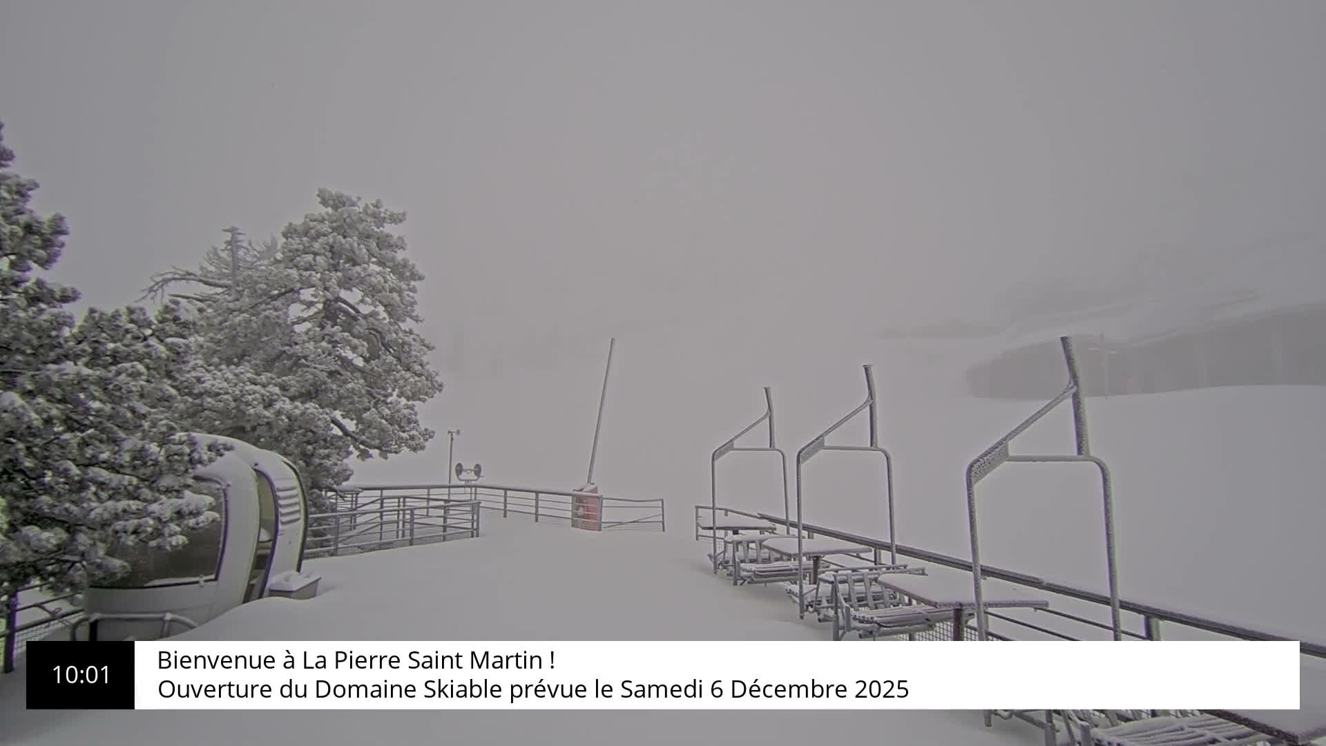 The image displays a snow-covered ski resort on an overcast and snowy day, featuring heavily laden pine trees, a gondola cabin, and several empty ski lift chairs extending into the foggy distance.