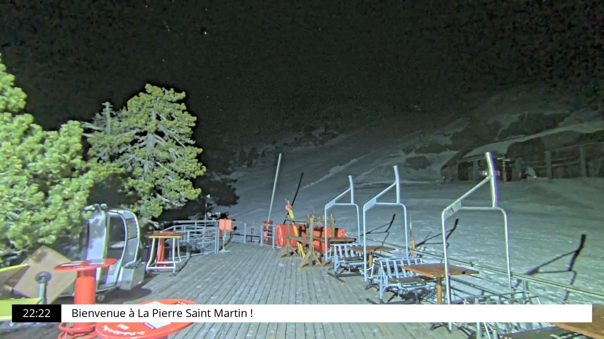 The image displays a snow-covered ski resort on an overcast and snowy day, featuring heavily laden pine trees, a gondola cabin, and several empty ski lift chairs extending into the foggy distance.