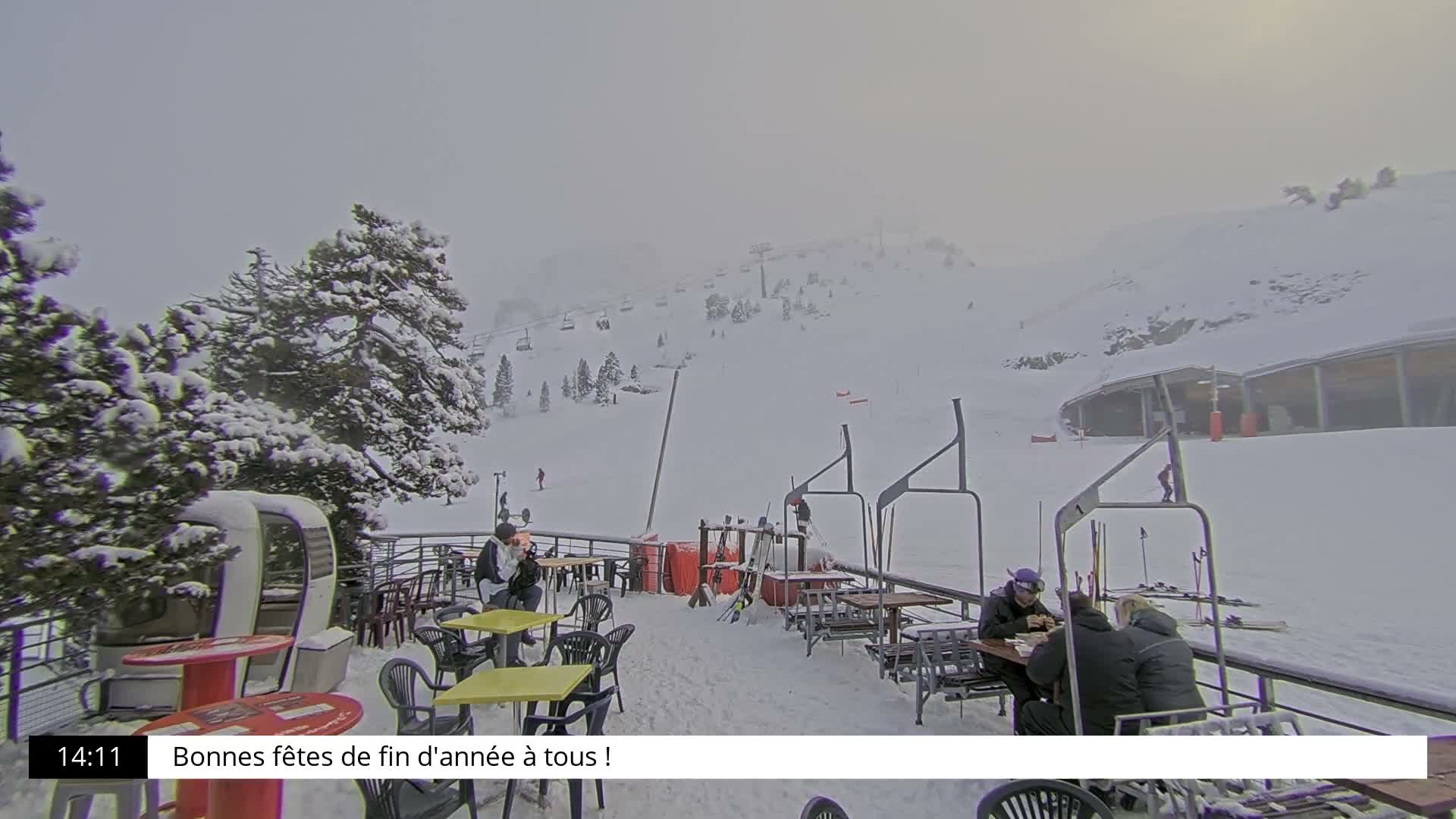 The image displays a snow-covered ski resort on an overcast and snowy day, featuring heavily laden pine trees, a gondola cabin, and several empty ski lift chairs extending into the foggy distance.