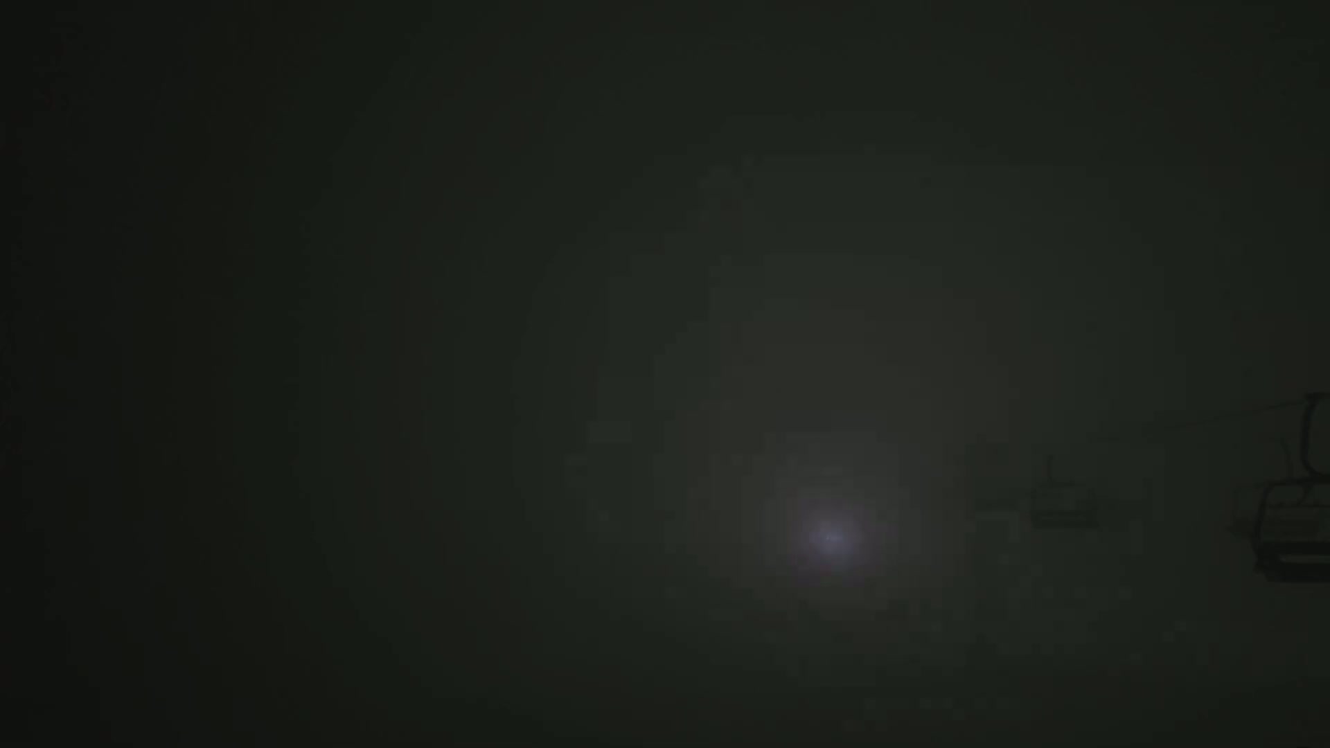 A dimly lit, foggy scene shows several chairlifts on a cable against a dark background.
