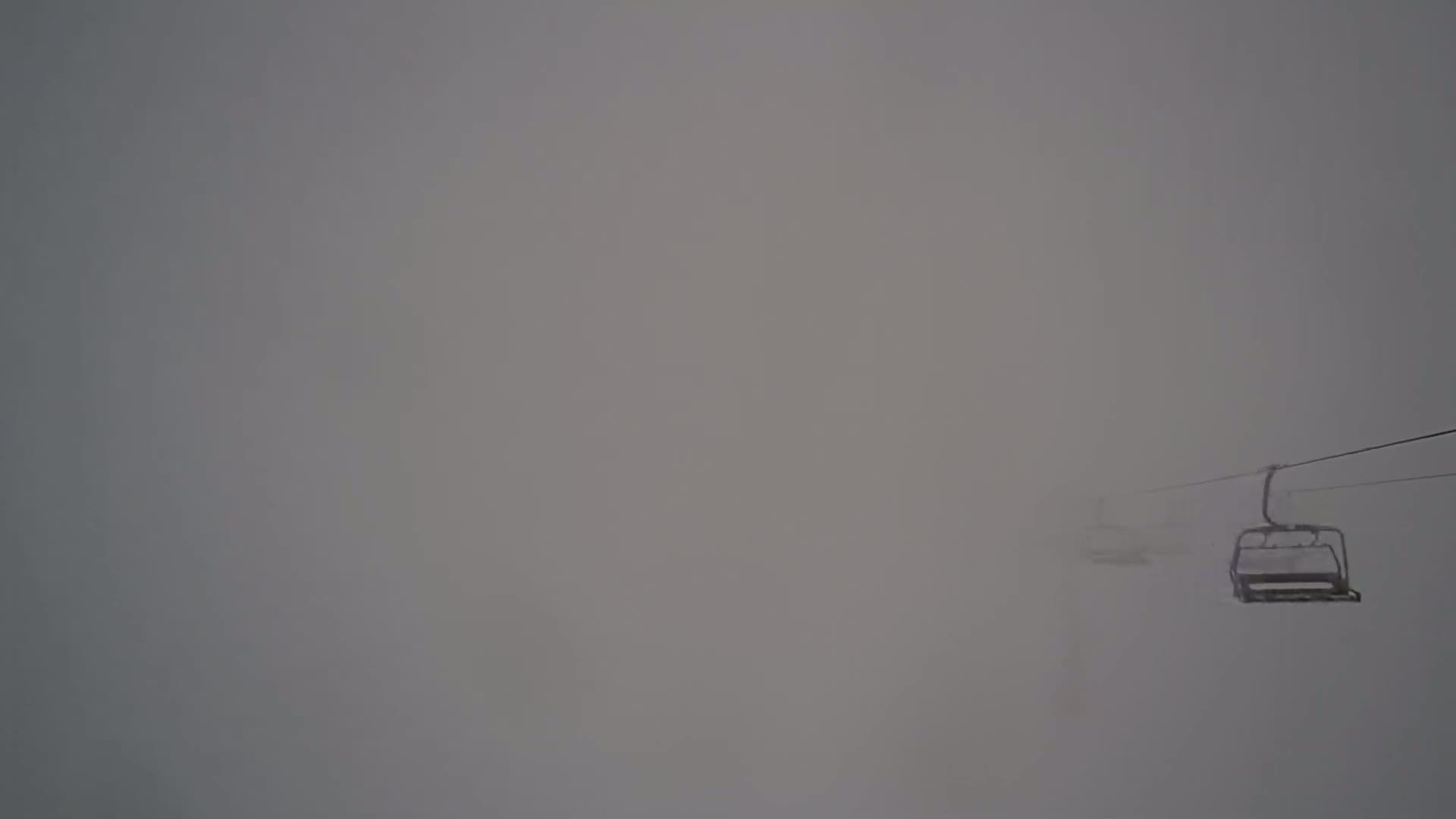 A chairlift moves through a thick fog.