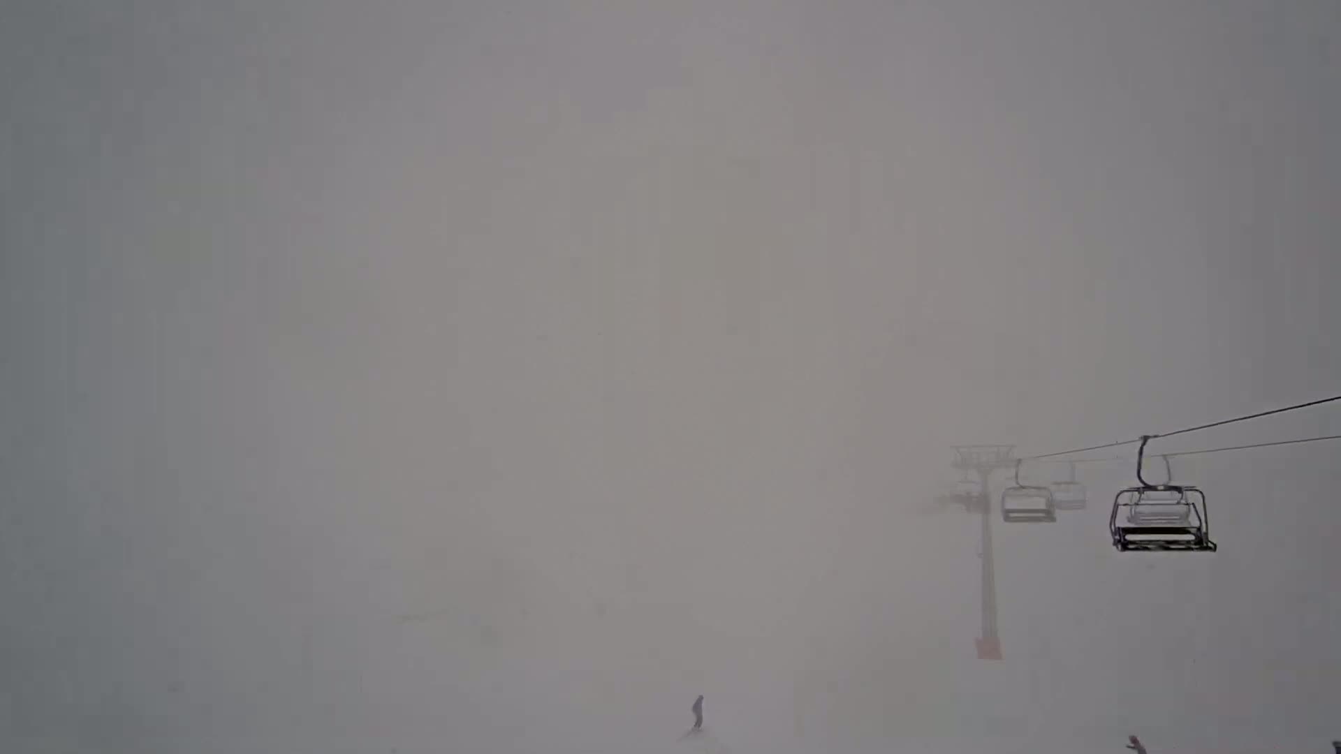 A ski lift with several empty chairs ascends into a dense fog on a snowy mountainside.