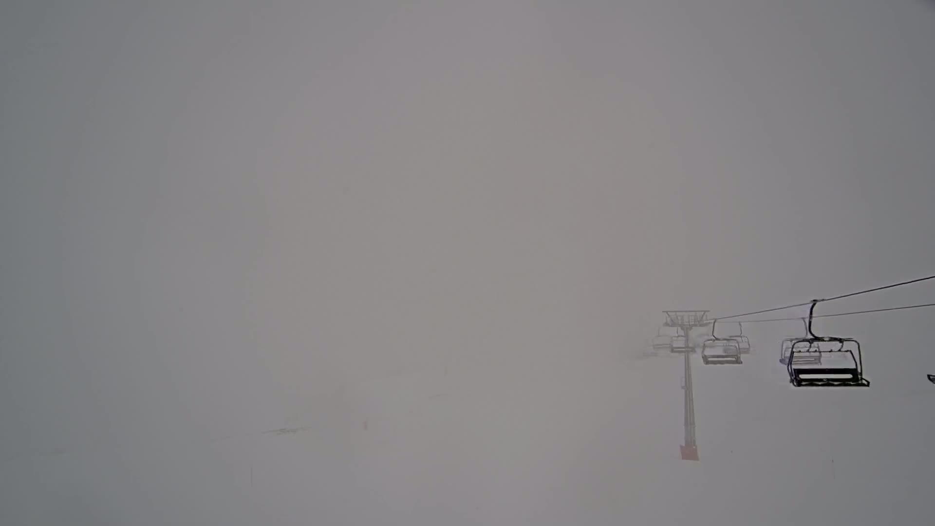 A ski lift with several empty chairs extends into a dense fog over a snow-covered landscape.