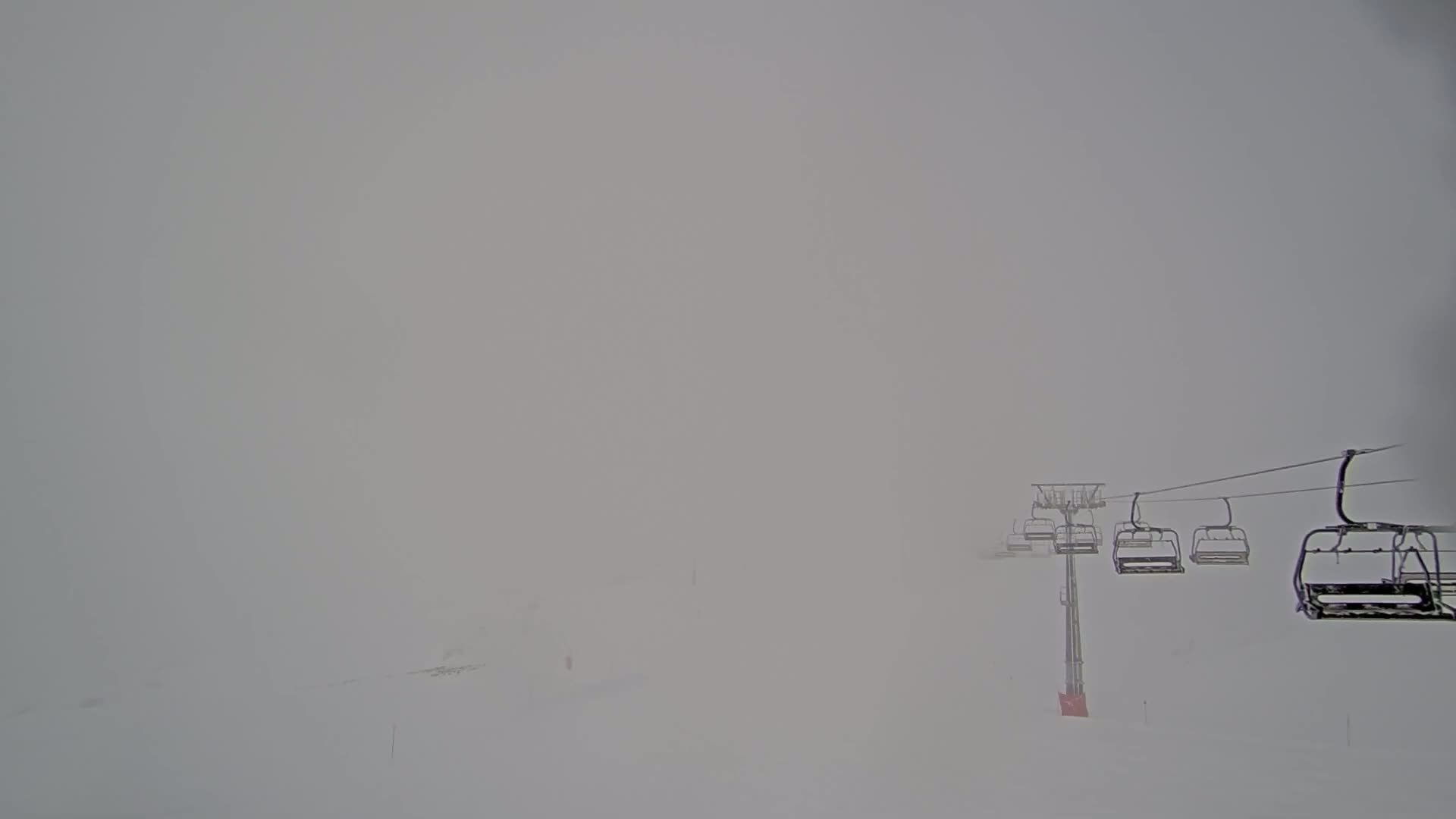 A chairlift ascends a snow-covered slope in heavy fog.
