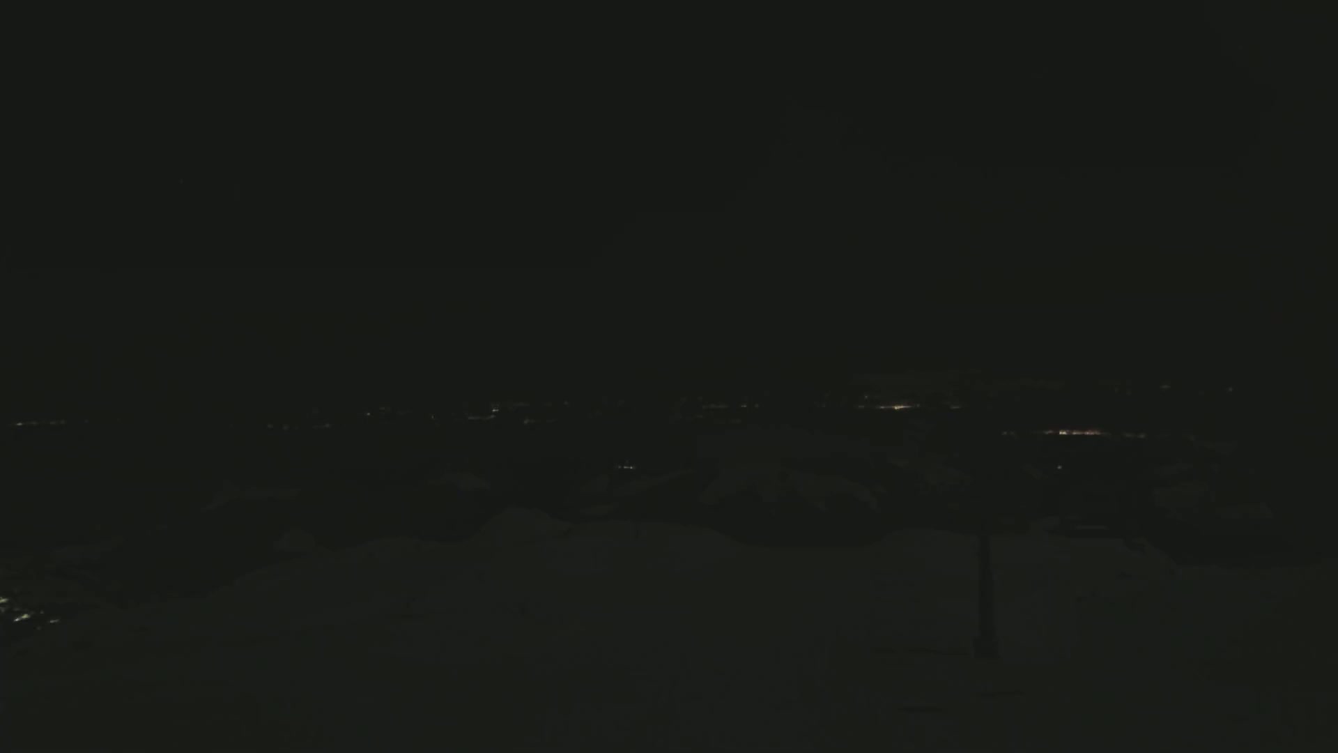 A dark, snowy landscape at night shows a distant city glowing faintly on the horizon.