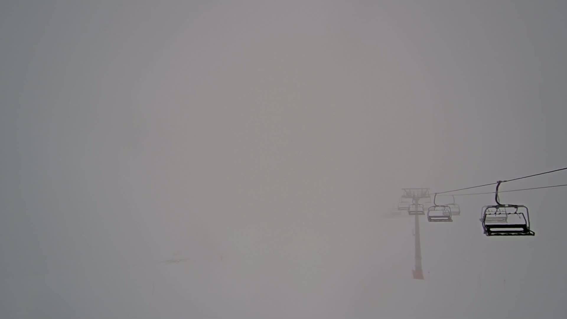 A chairlift with several empty chairs ascends through a thick fog.