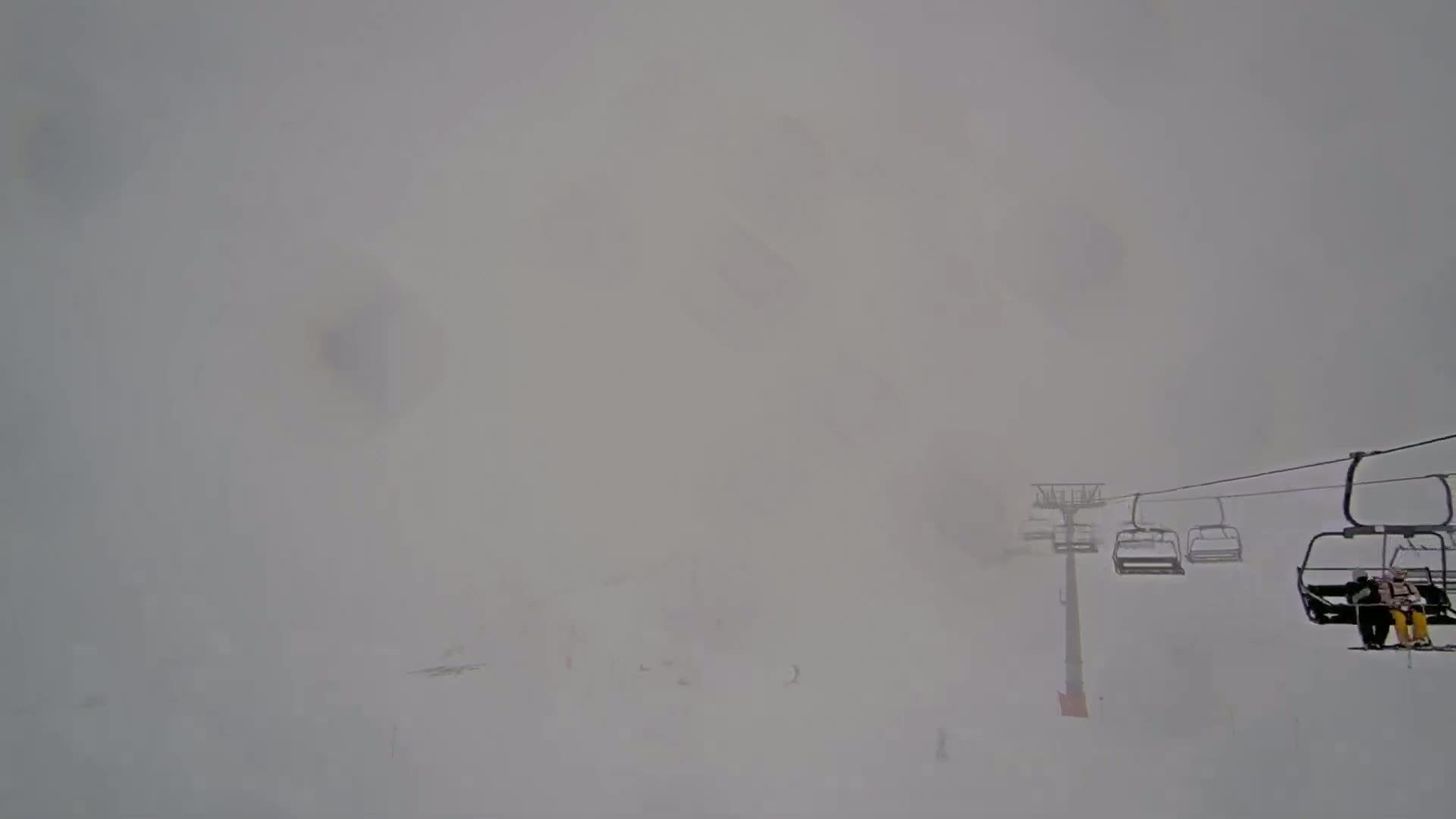 A chairlift carrying skiers ascends through a thick fog on a snowy mountain slope.