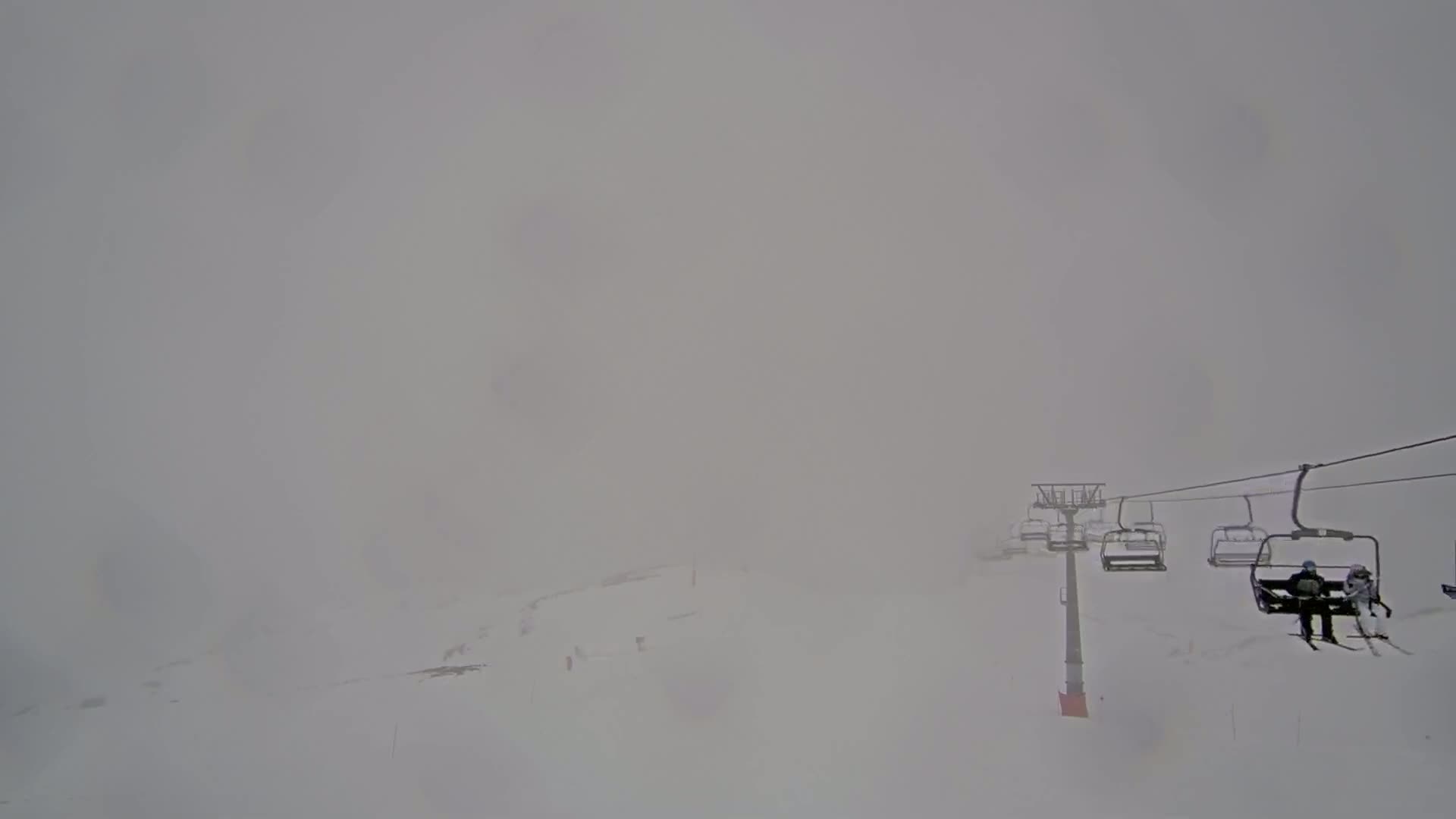 A chairlift carrying skiers ascends a snow-covered slope in heavy fog.