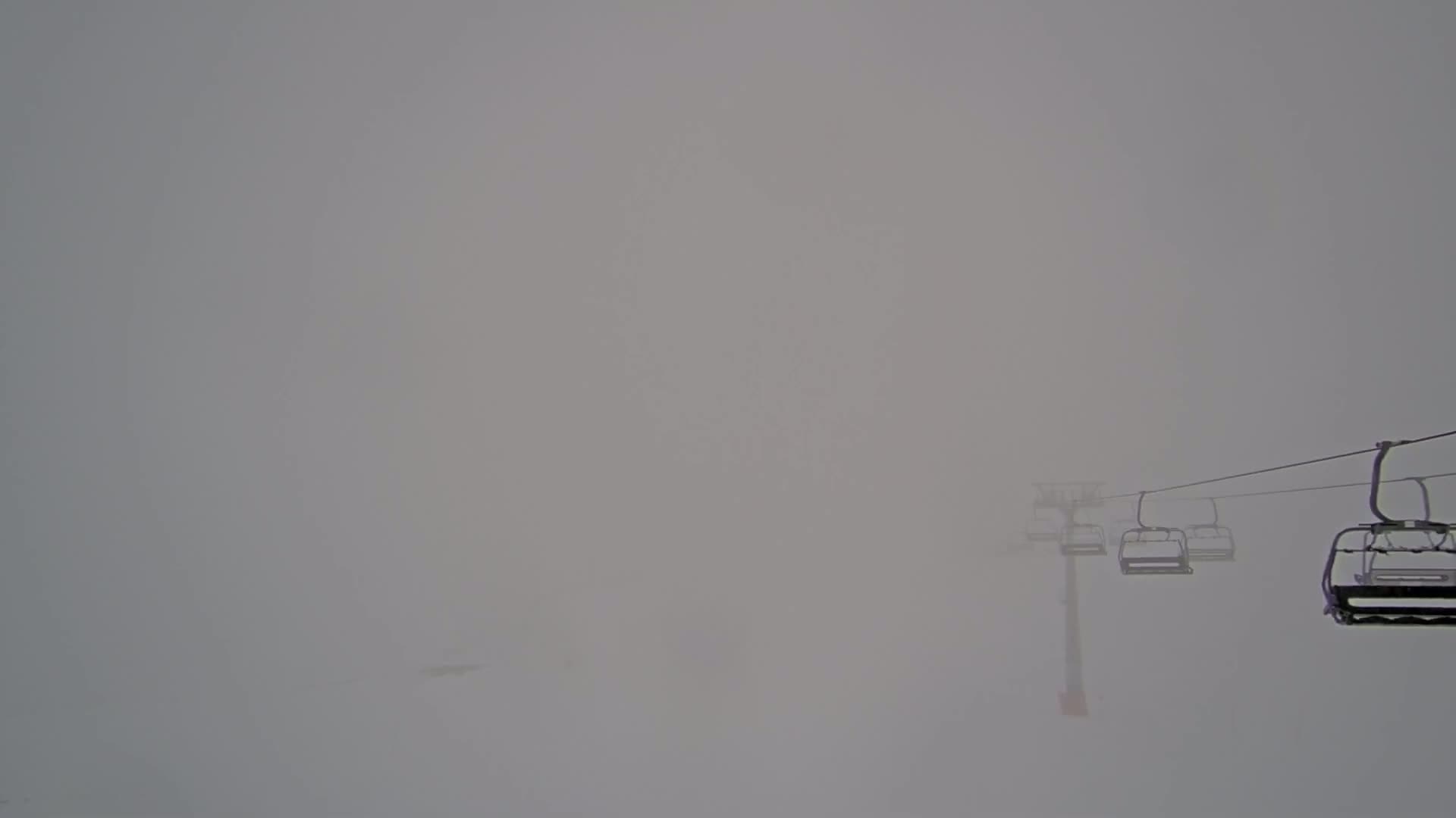 A chairlift extends into a dense fog on a snowy landscape.
