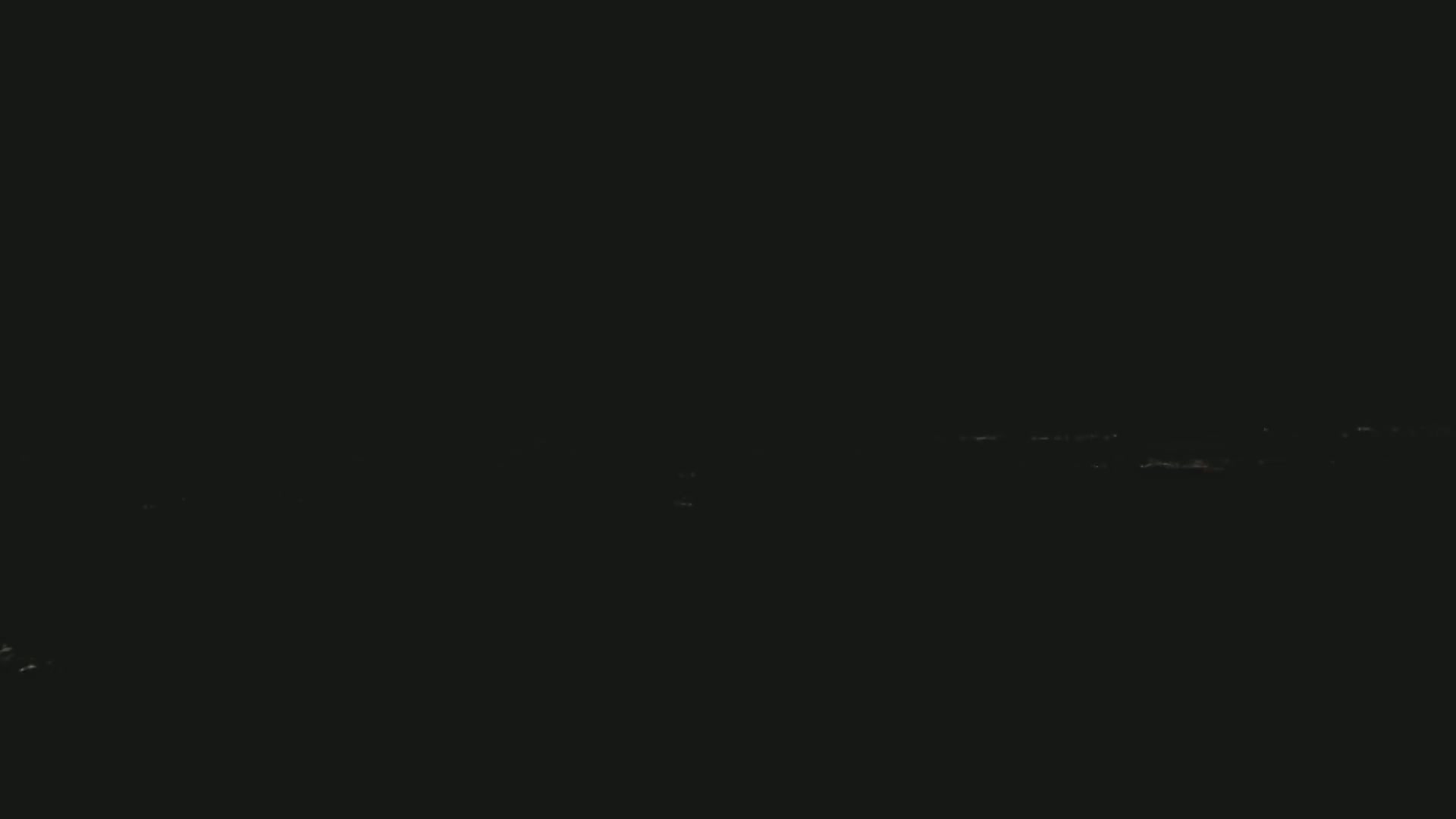 A dark, nighttime scene shows a faint, distant line of lights on the horizon.