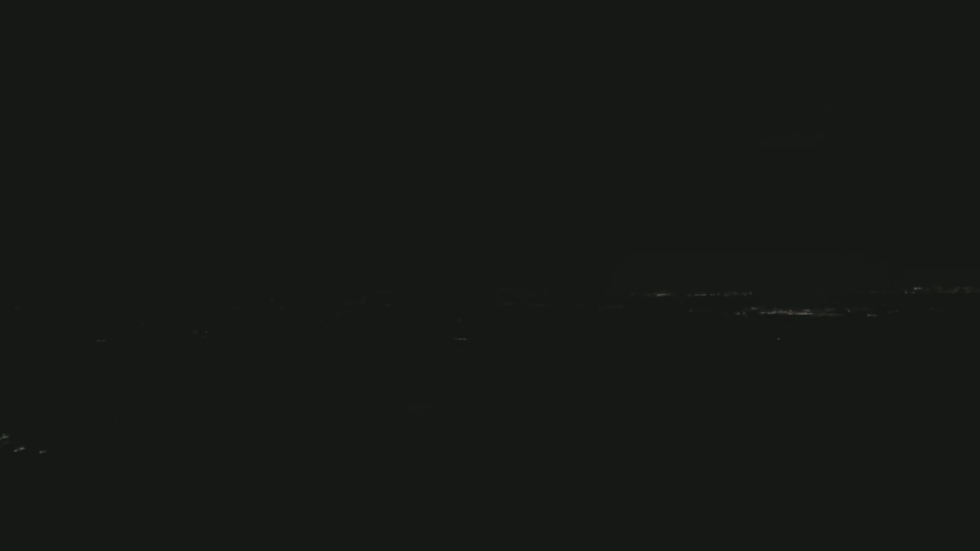 A distant cityscape is faintly visible at night under a dark, clear sky.