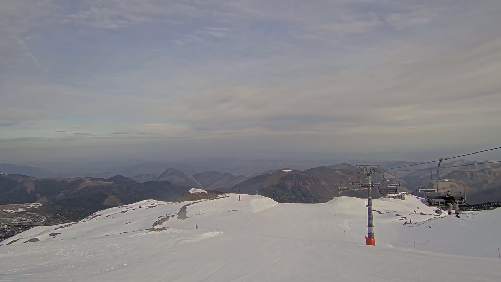 A chairlift ascends a snow-covered mountain range under a cloudy sky.