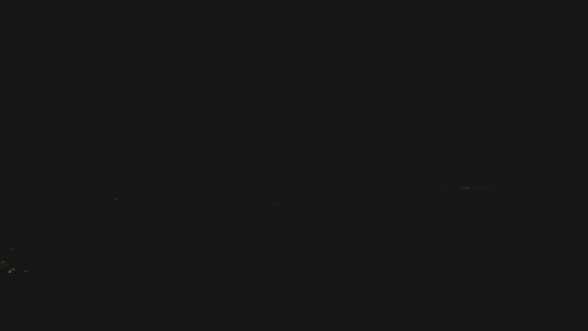 A dark, nighttime scene shows a few faint lights in the distance on a seemingly clear night.