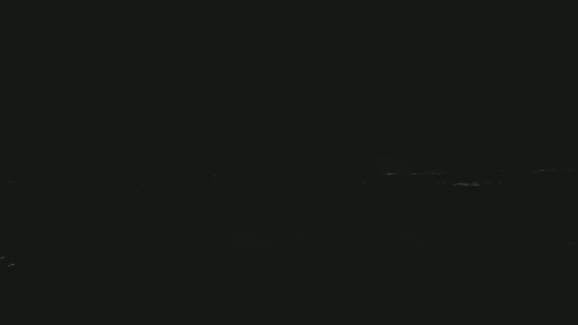 A dark, nighttime scene shows a faint line of distant lights on the horizon.