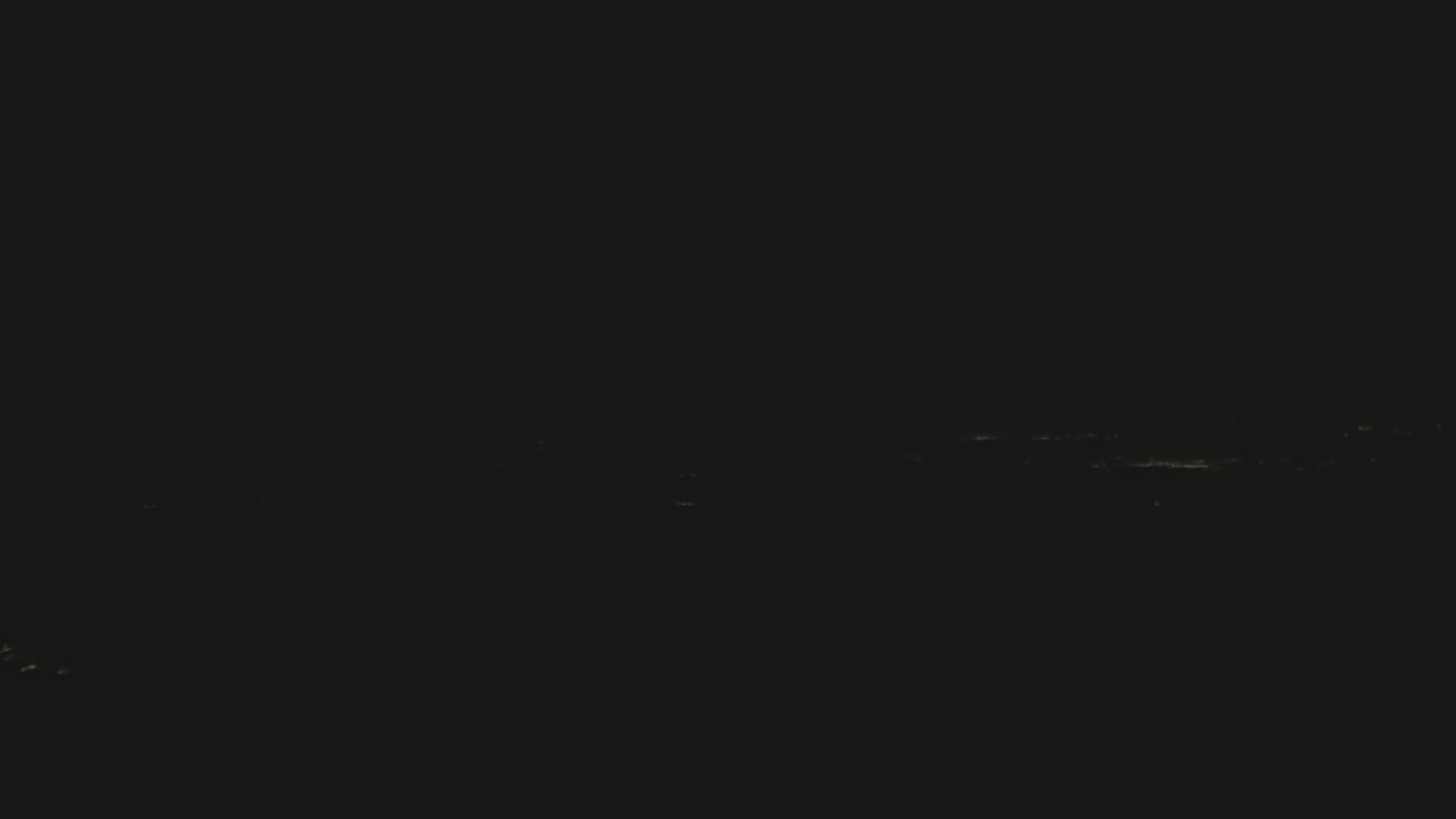 A dark, nighttime scene shows a distant line of faint lights on a dark horizon.