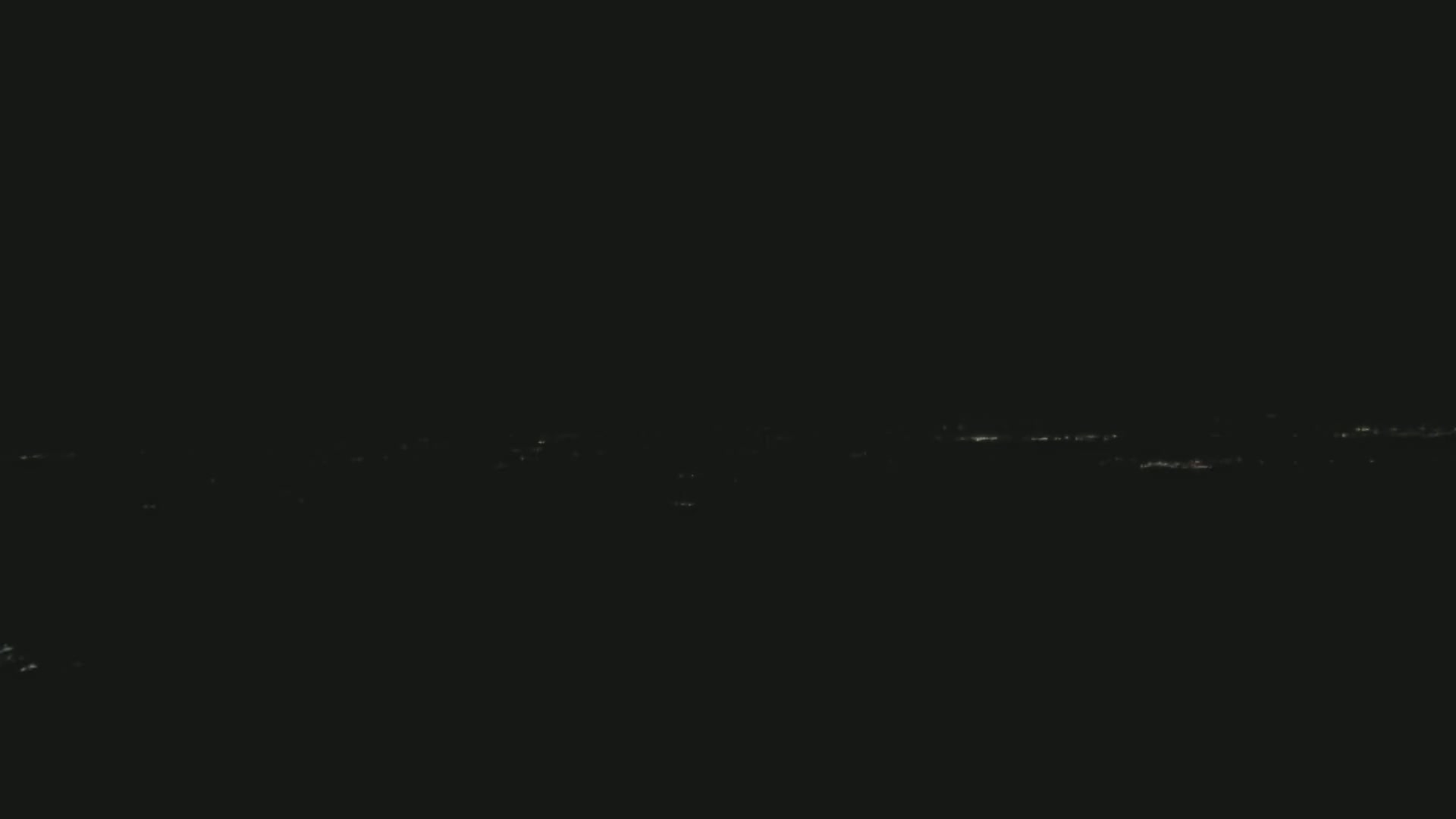 A long, thin line of faint lights stretches across a dark, nighttime landscape.