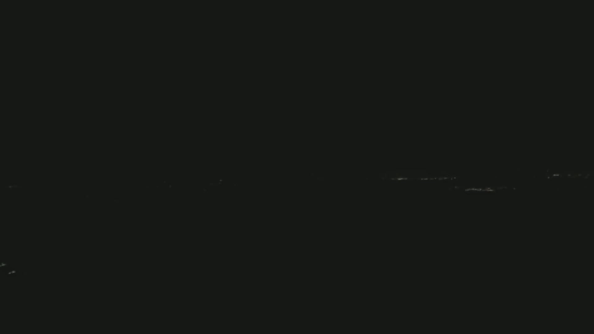 A dark nighttime scene shows a faint line of distant city lights on the horizon.