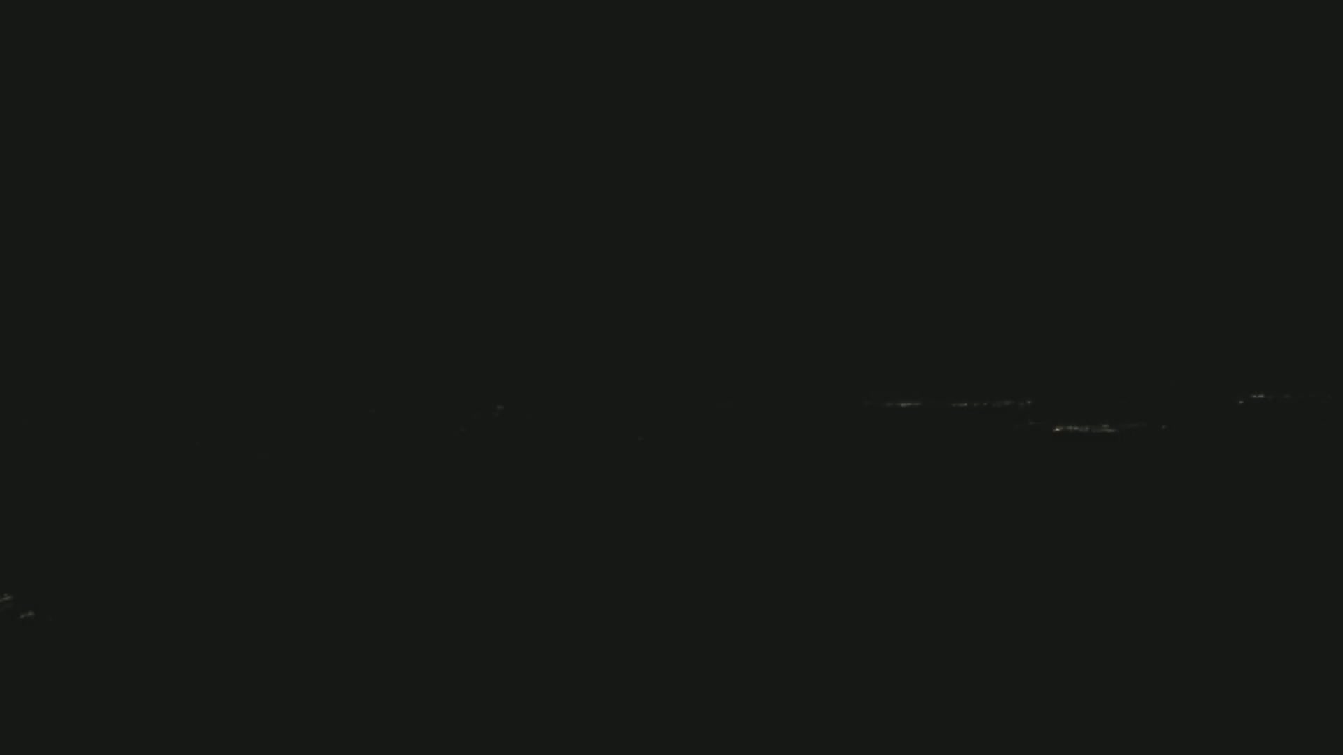 A nighttime, long-distance view shows a faint line of distant lights on the horizon.