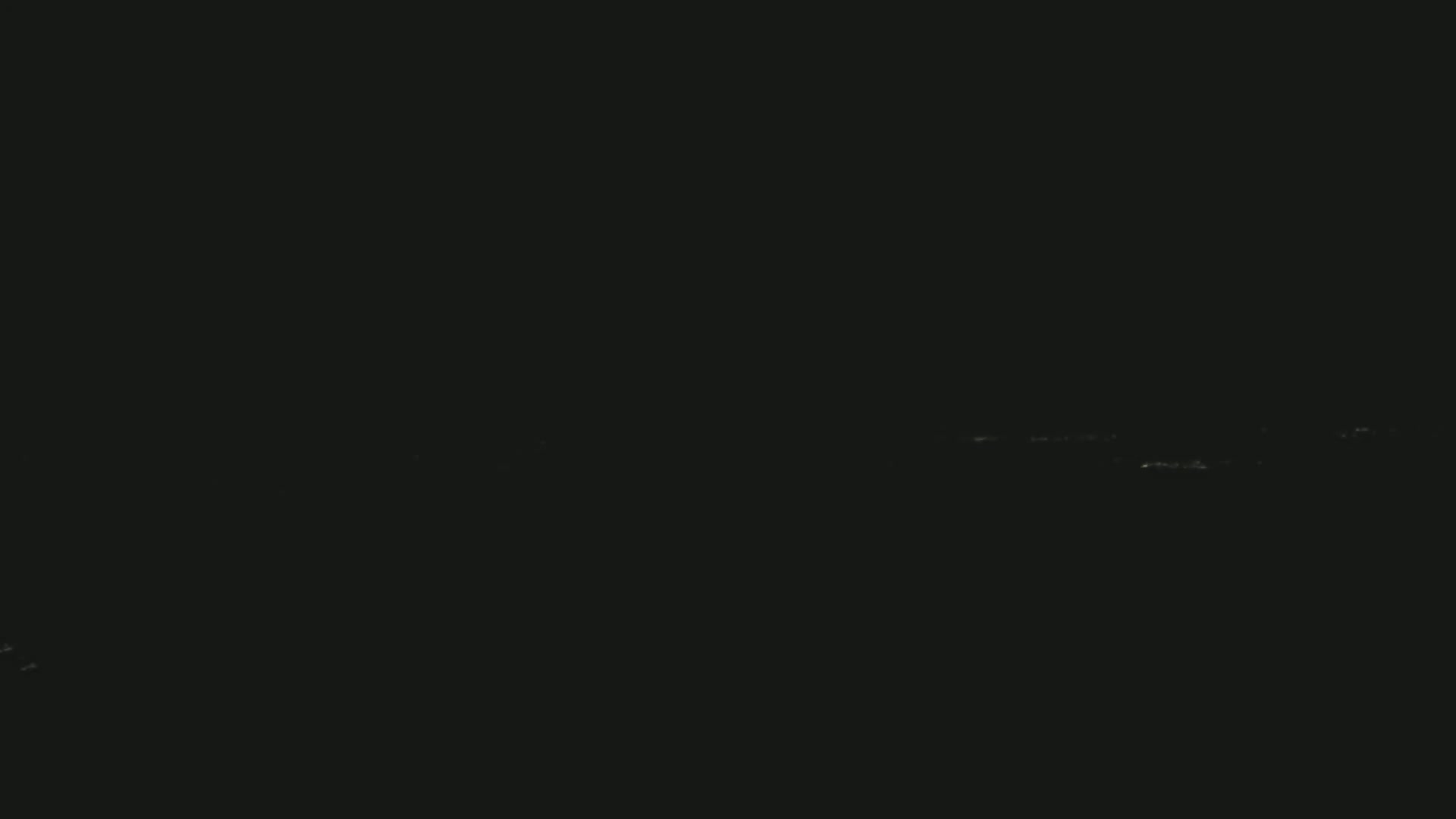 A dark, nighttime scene shows a faint, horizontal line of distant lights against a mostly black sky.
