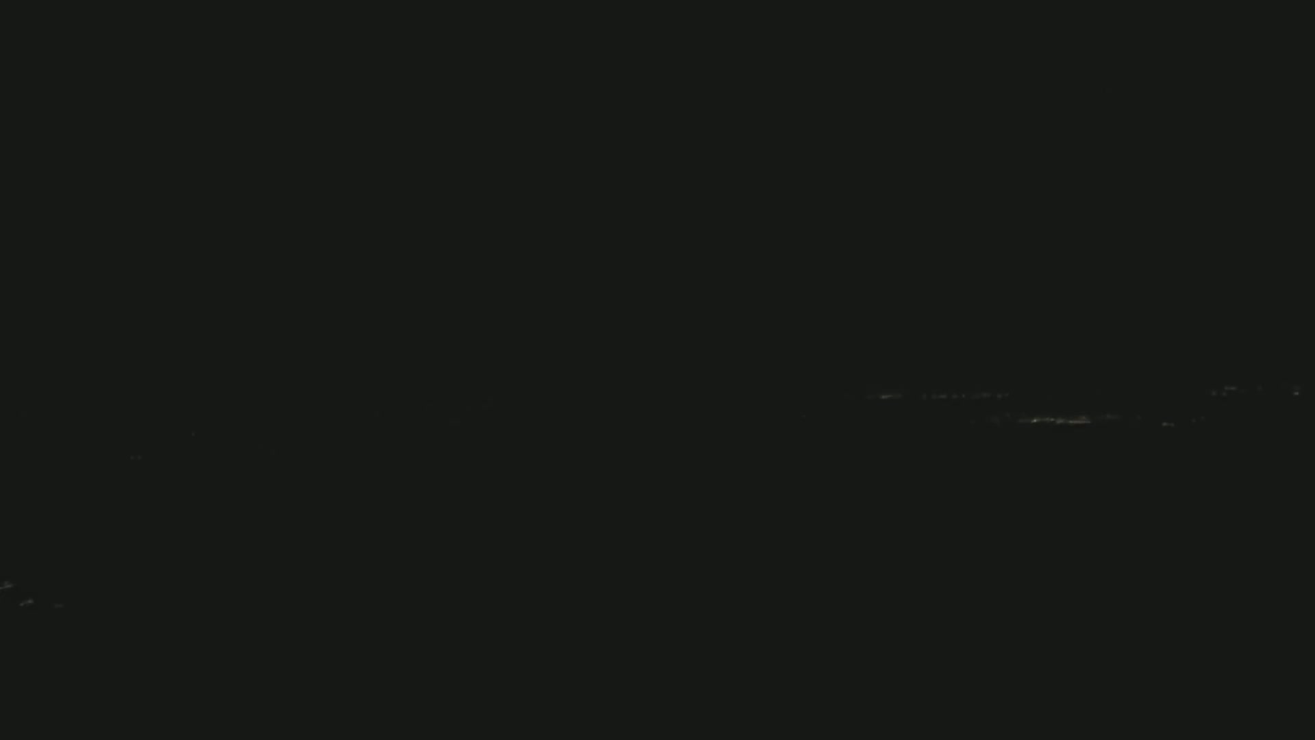 A dark, nighttime scene shows a faint, distant line of lights on the horizon.