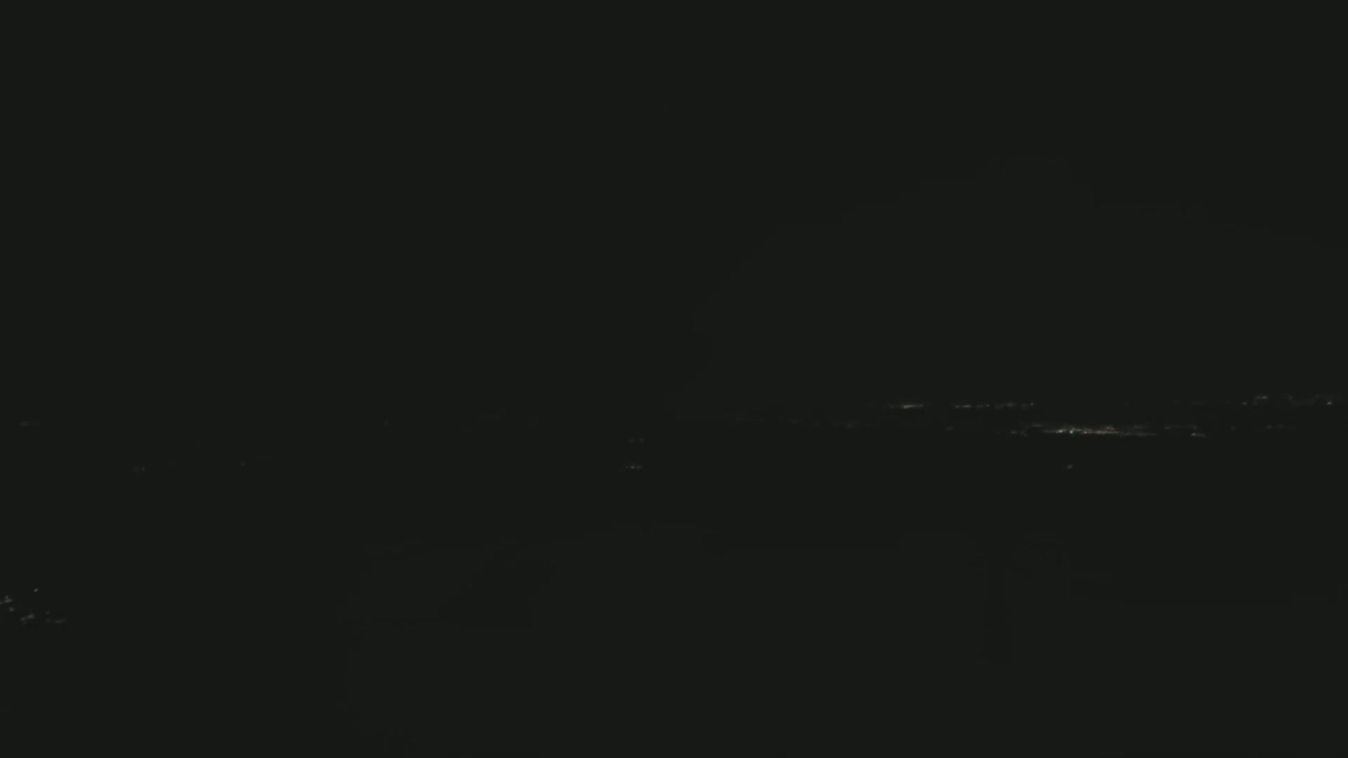 A dark, nighttime view shows a distant line of faint city lights.