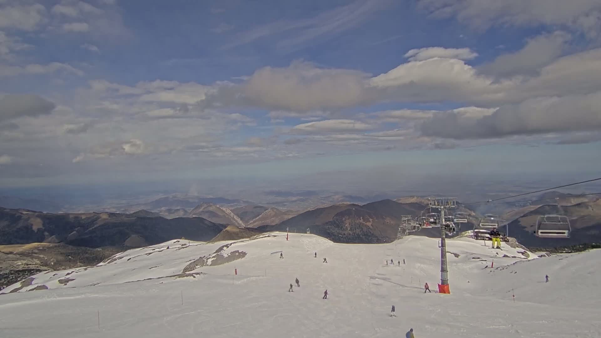 A snow-covered mountain slope with skiers and a chairlift under a partly cloudy sky.